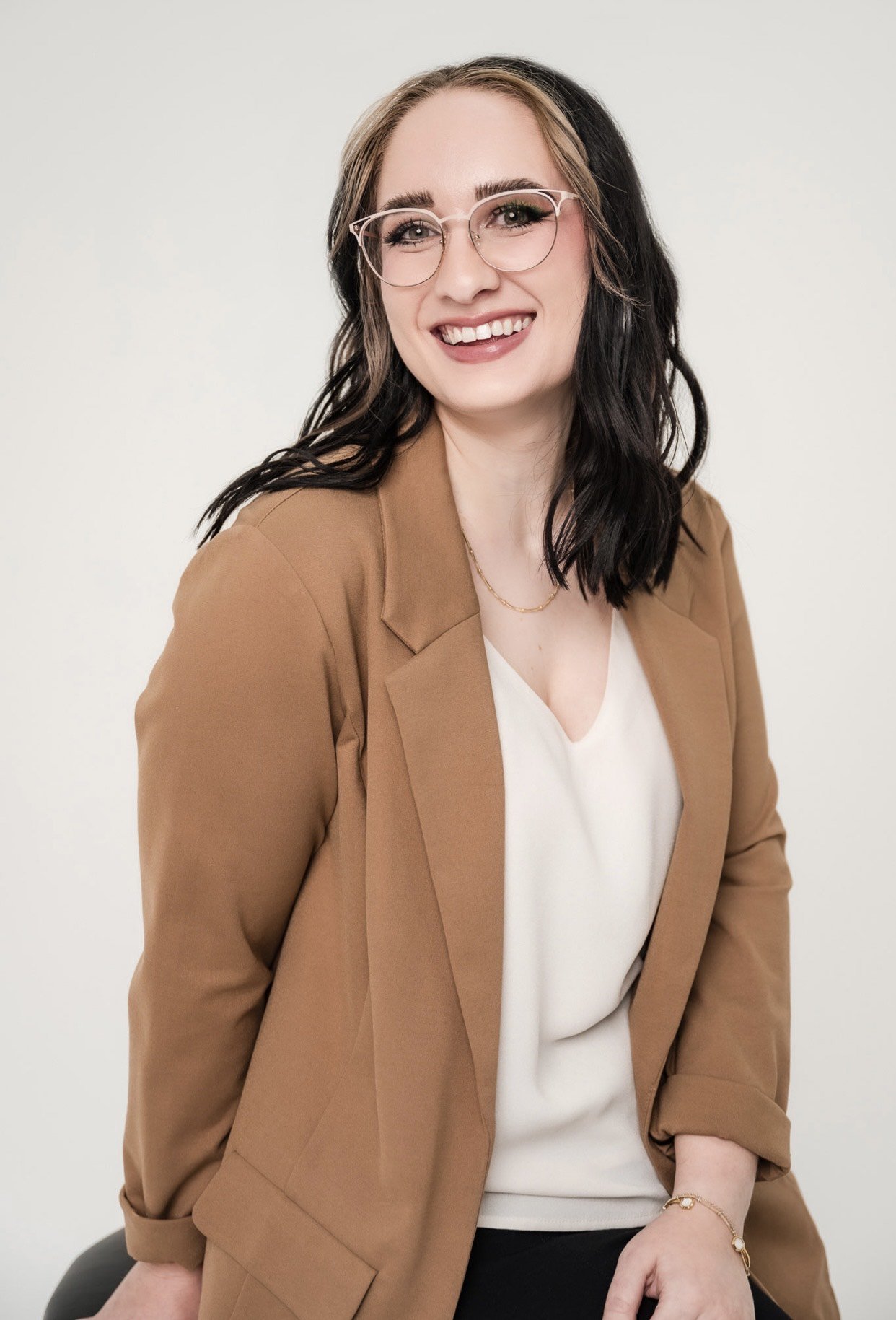 Smiling person with glasses, brown blazer, and white top
