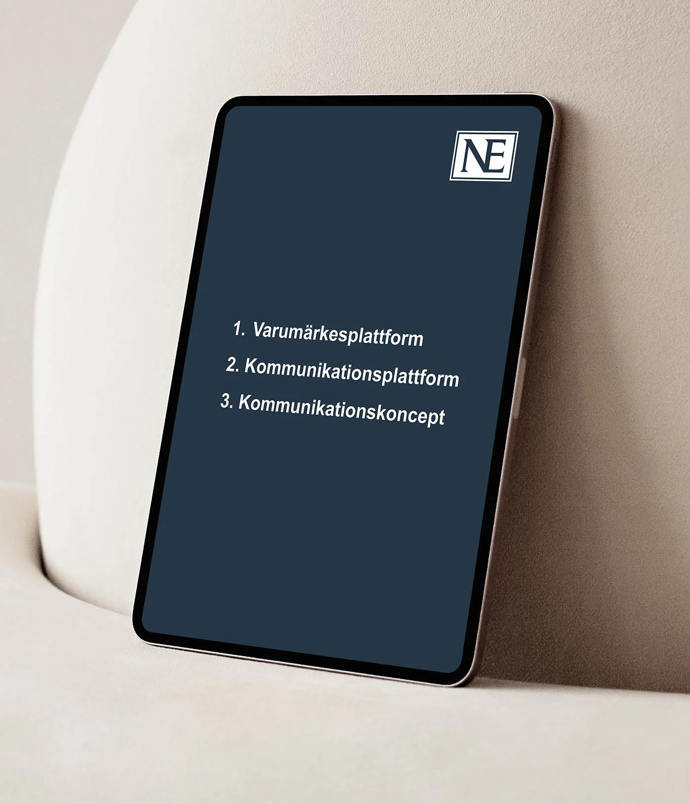 En mobiltelefon som visar en lista med tre punkter, texten är på svenska: 1. Varumärkesplattform, 2. Kommunikationsplattform, 3. Kommunikationskoncept, och ett NE-logotyp i övre högra hörnet.