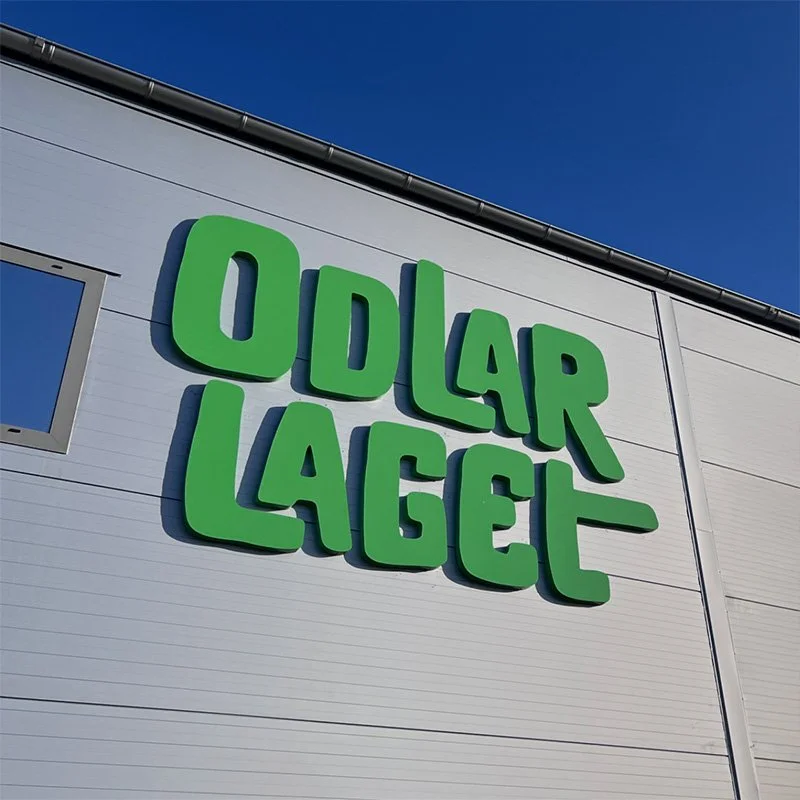 Bild av ett lager och kontor med en stor grön skylt som säger 'Odlarlaget' på en grå byggnad under en klar blå himmel i Helsingborg.