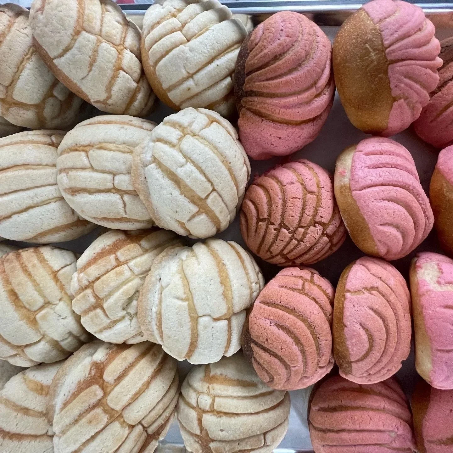 Assorted cookies with pink and white sugar cookies, some with striped patterns, arranged in rows.