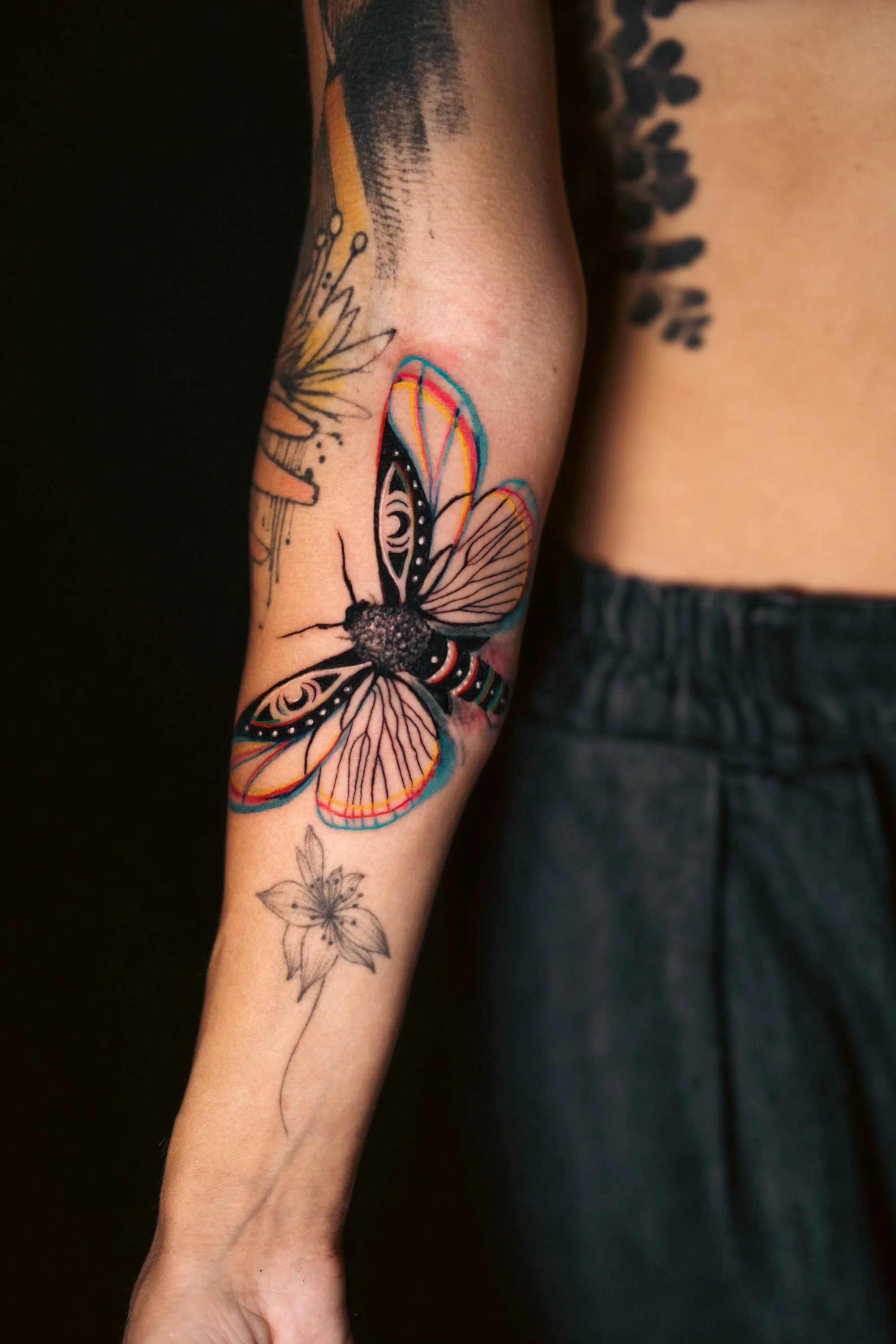 Colorful glitch moth tattoo on forearm, with floral and abstract designs.