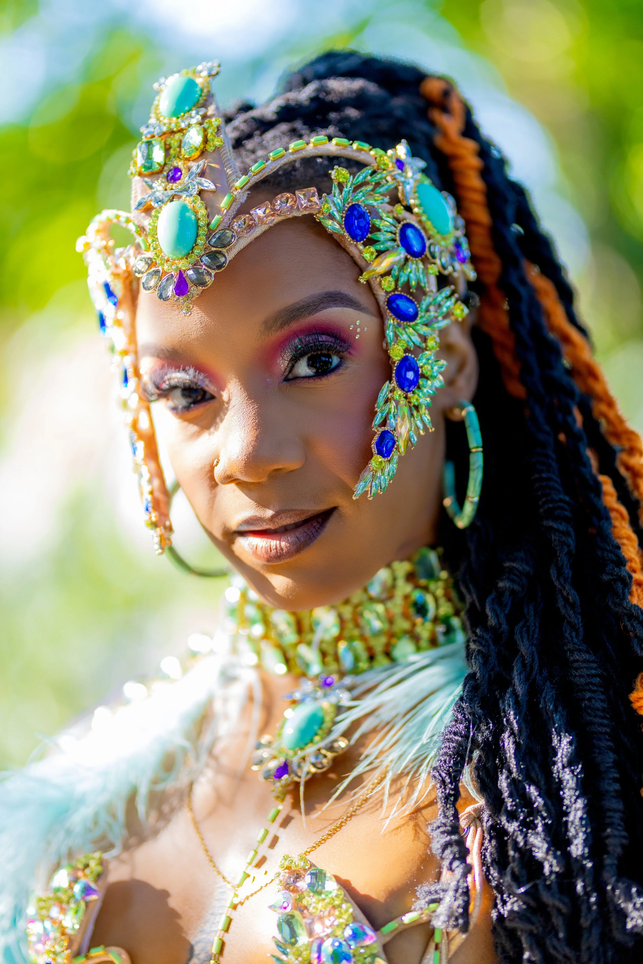 A woman wearing elaborate colorful jewelry and a decorative headpiece, with a blurred green background.
