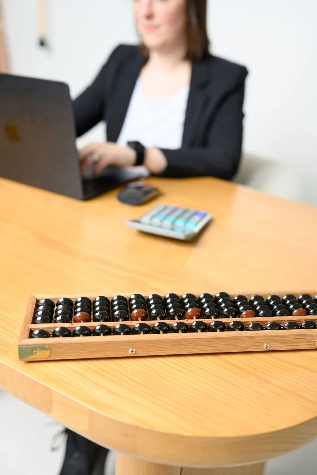 A woman working at a desk with a laptop and calculator, with an abacus in the foreground.