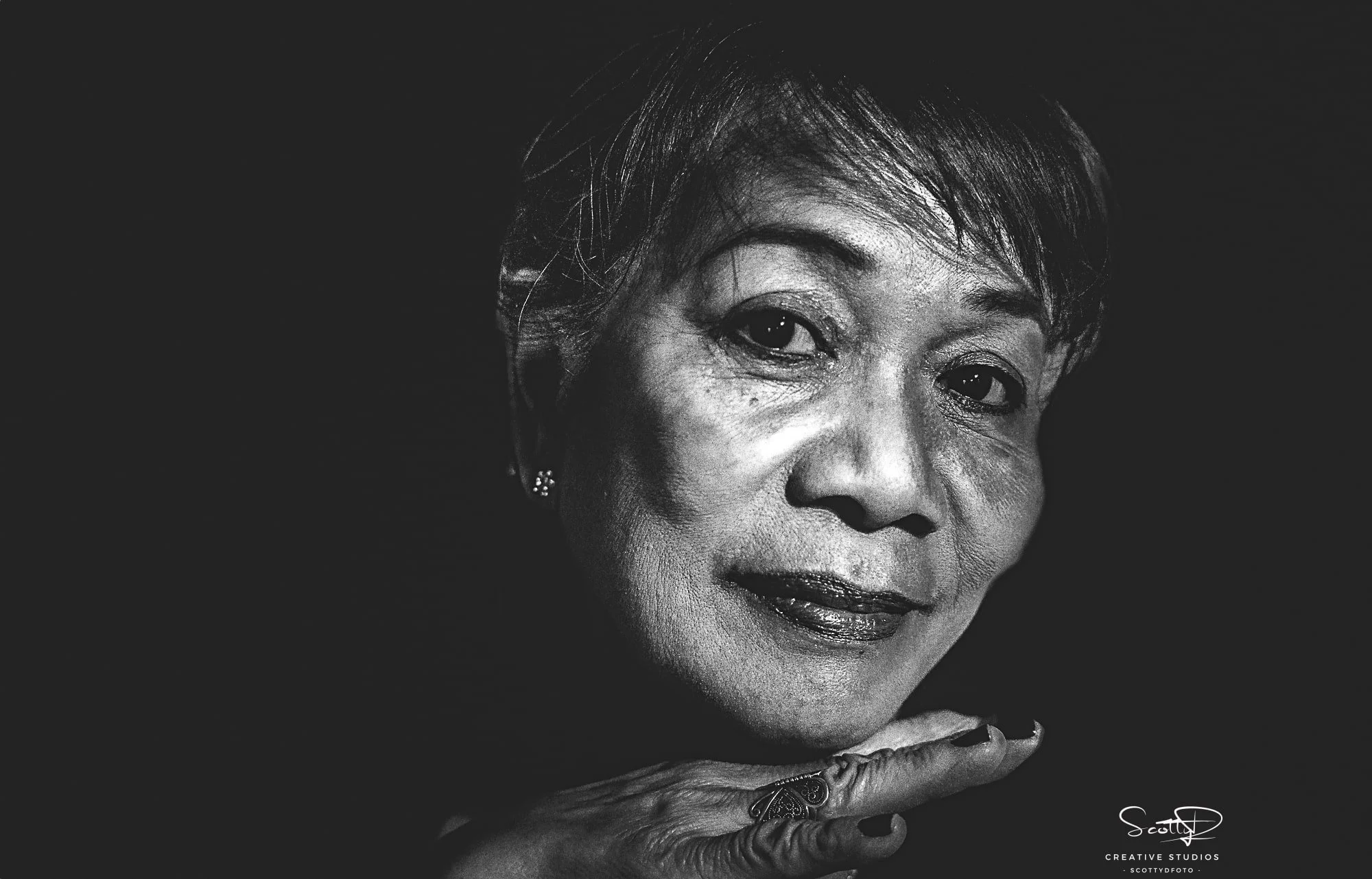 Black and white portrait of an older woman with hand under chin, highlighted by the invisible black background technique using a single flash. Photo by ScottyD, ScottyDfoto, Scottyd Creative Studios.  Dayton, Ohio.