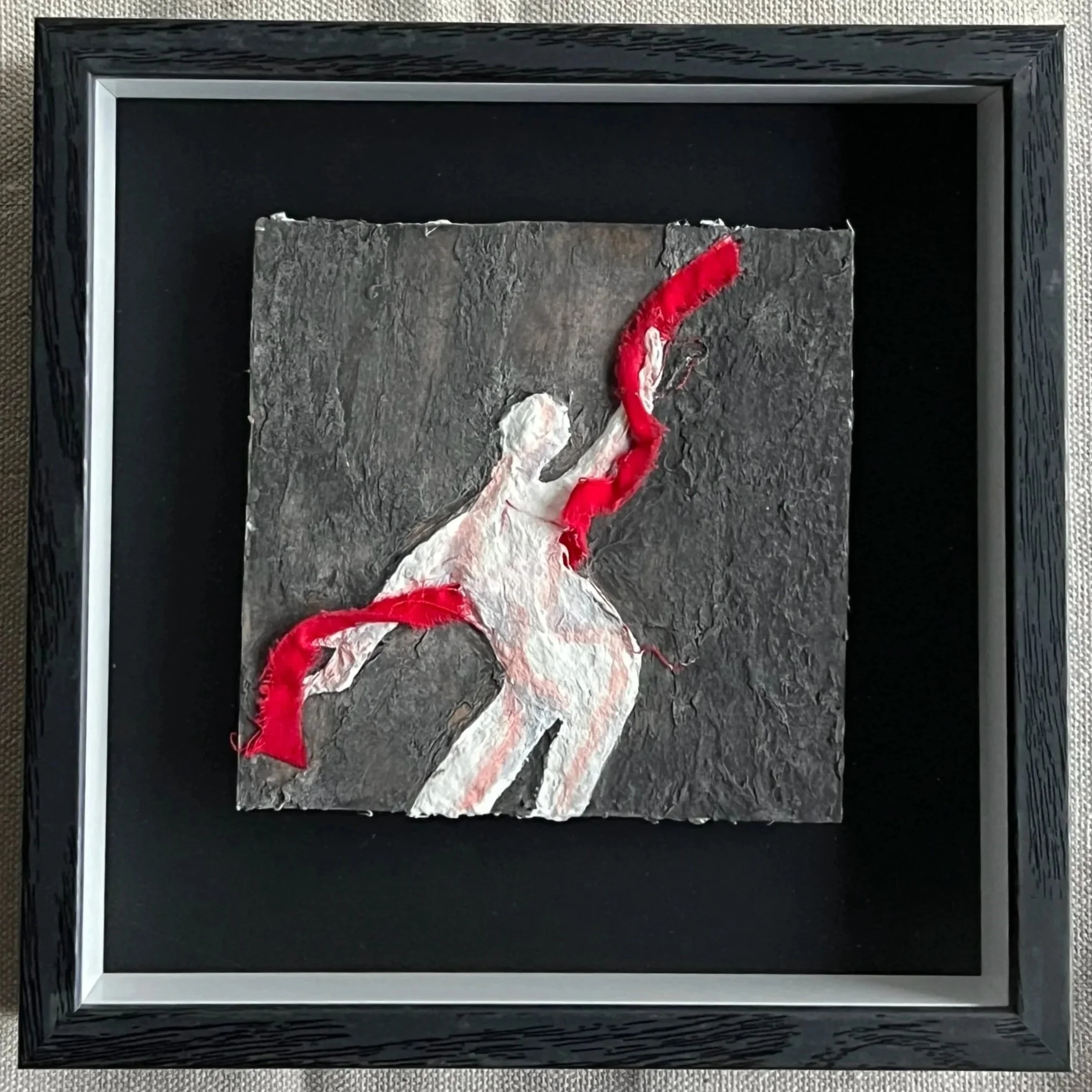 Small mixed media artwork featuring an abstract white female figure in motion against a dark gray background, intersected by a vivid red ribbon-like form.