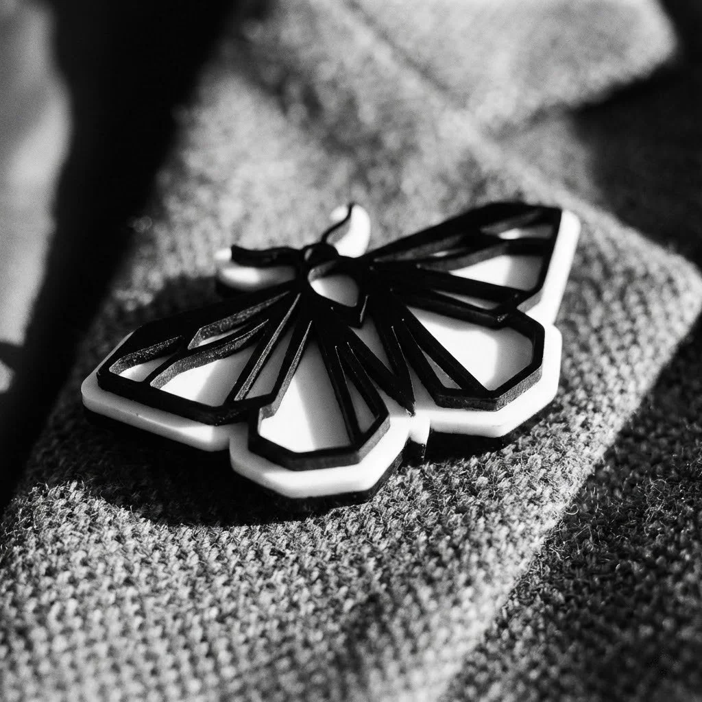 A black and white photo of a butterfly-shaped accessory, likely a brooch, placed on a textured fabric surface.
