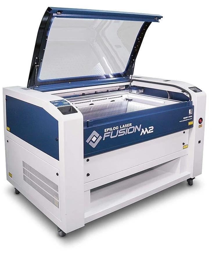 Industrial laser cutting machine labeled Epilog Laser Fusion M2 with a large enclosed work area and a transparent lid, used for cutting or engraving materials.