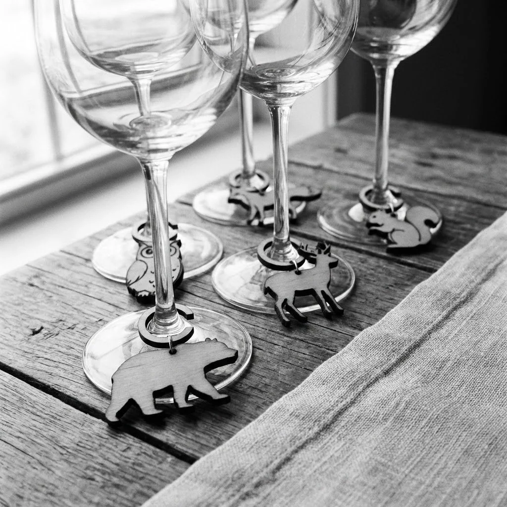 Four empty wine glasses with wooden animal-shaped wine charms on a rustic wooden table next to a cloth napkin.