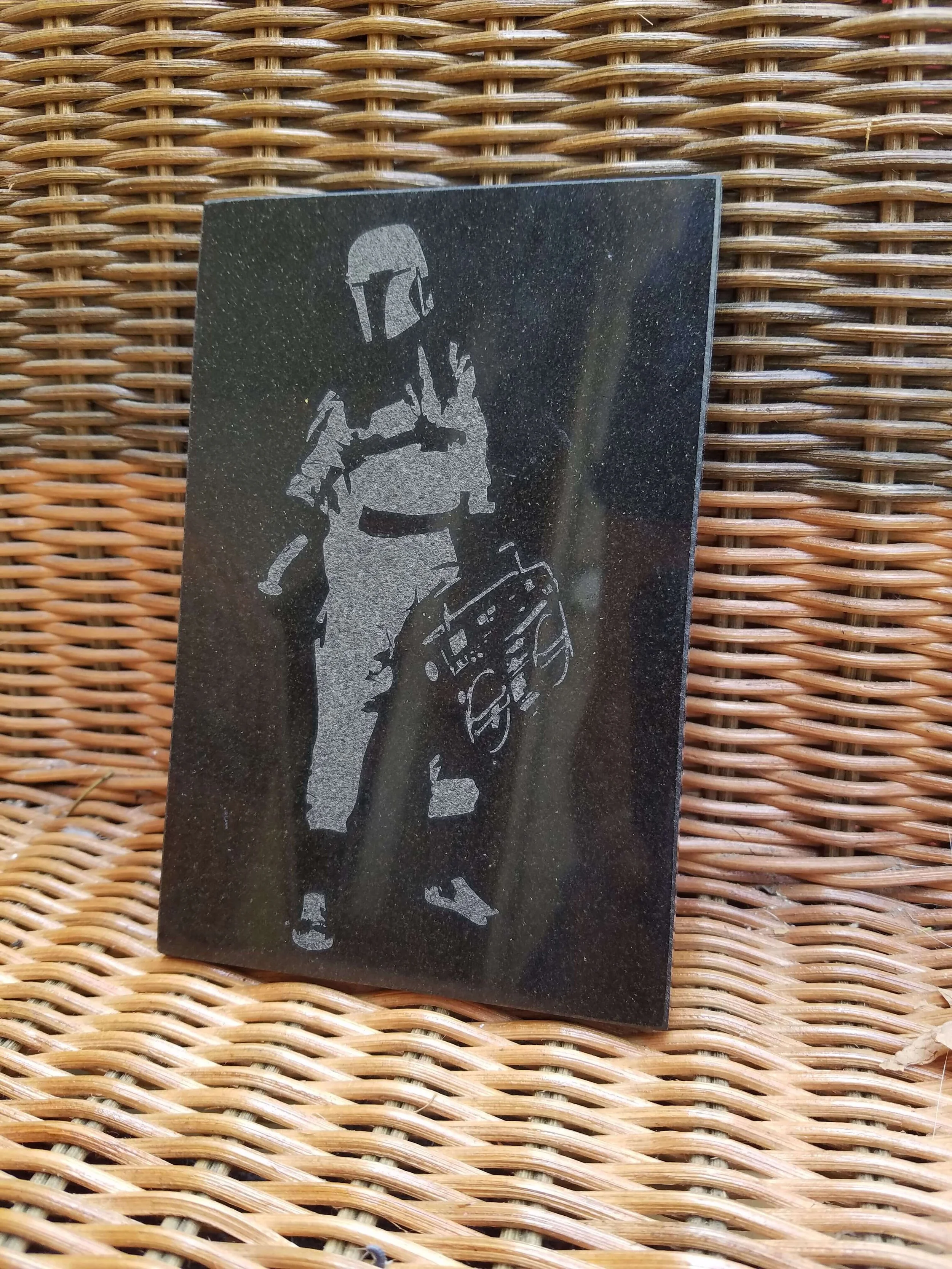 A black plaque with a silver silhouette of Boba Fett from Star Wars standing next to a speeder bike.