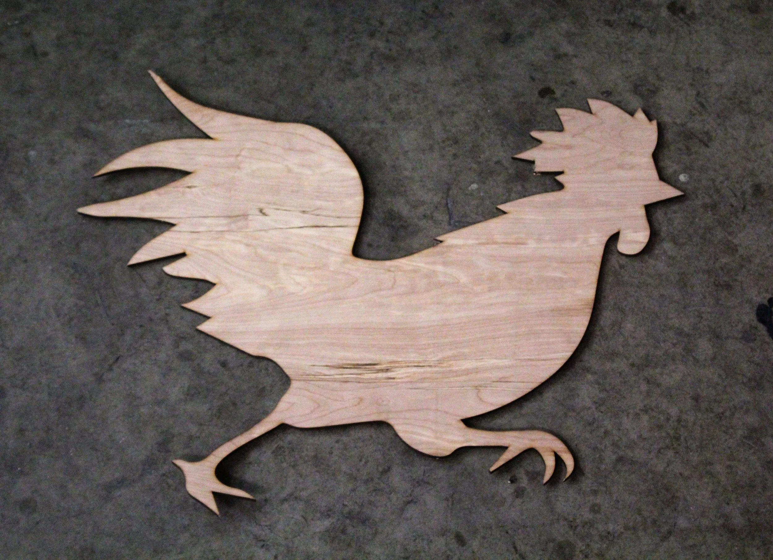 Wooden silhouette of a rooster on a concrete surface.