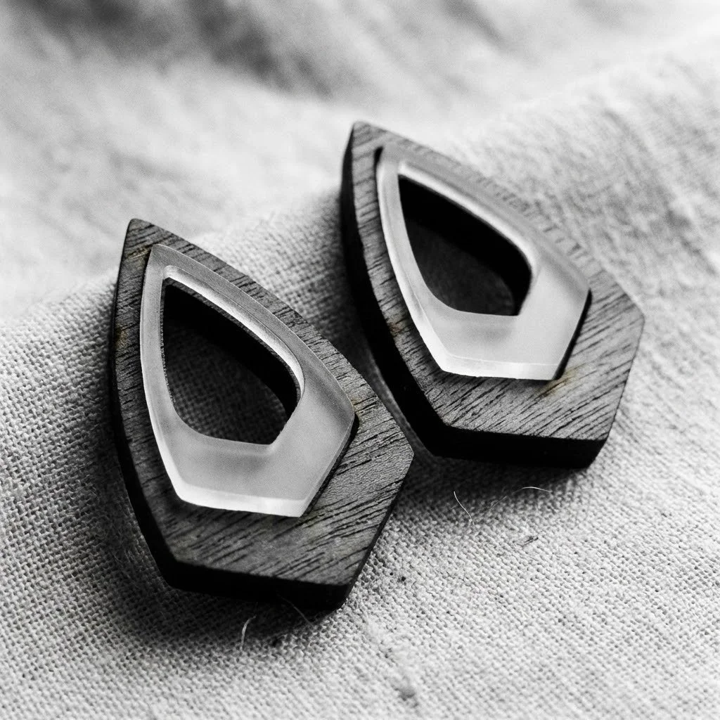 Pair of geometric earrings with wooden bases and metal accents on fabric surface in black and white.