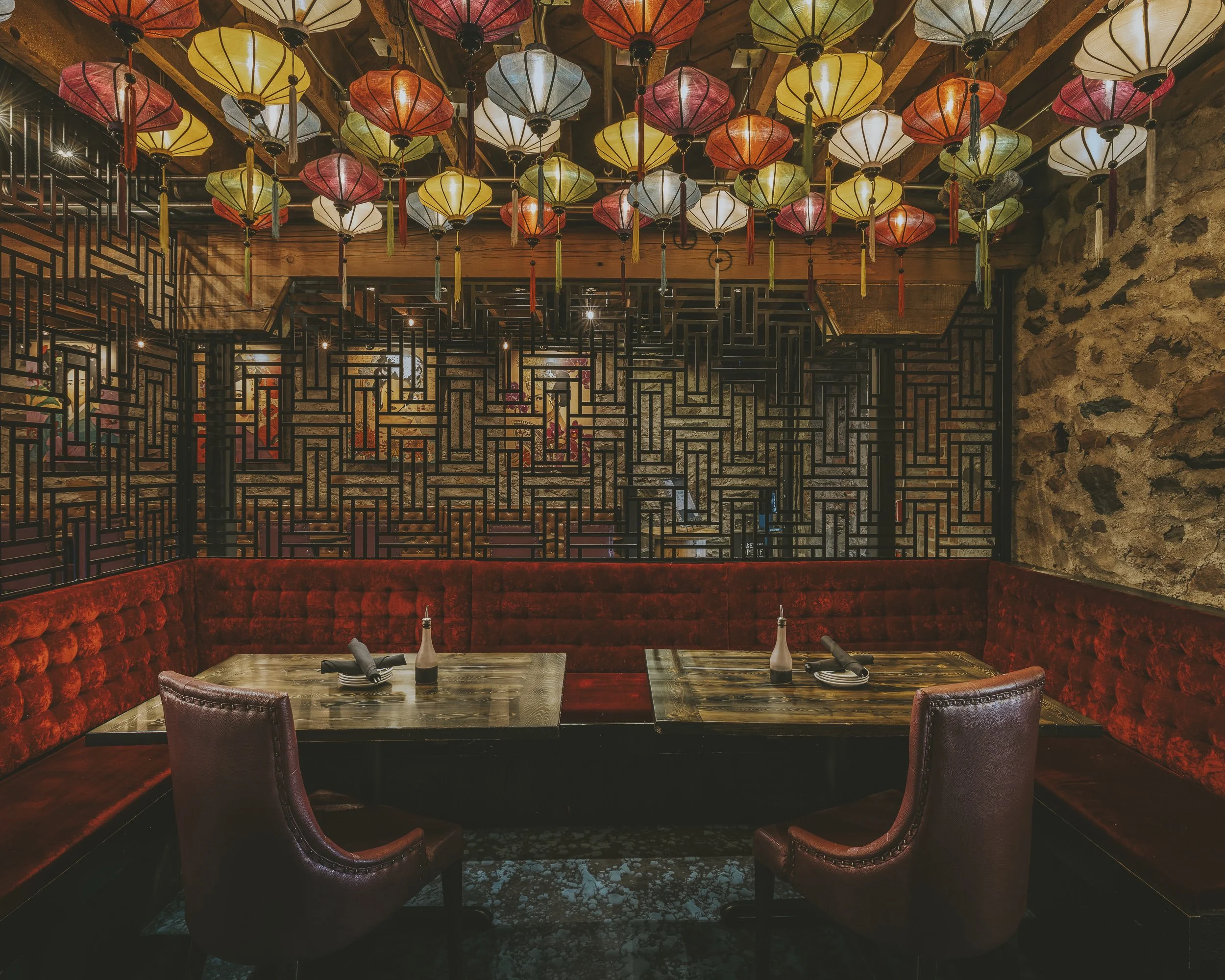 Interior of a restaurant with two tables, red upholstered seating, chairs, and decorative hanging paper lanterns