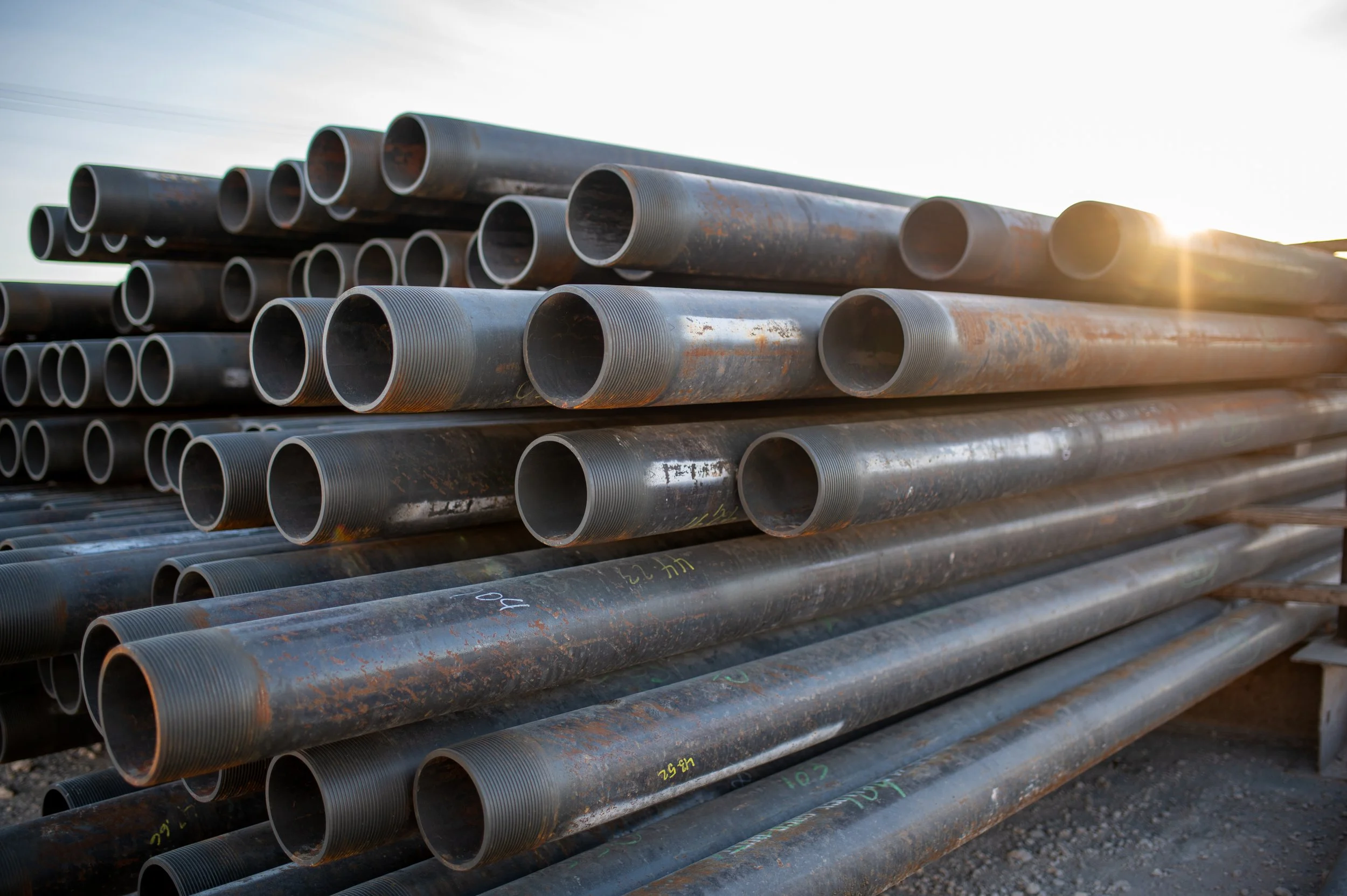 Stack of rusted metal pipes outdoors at sunset.