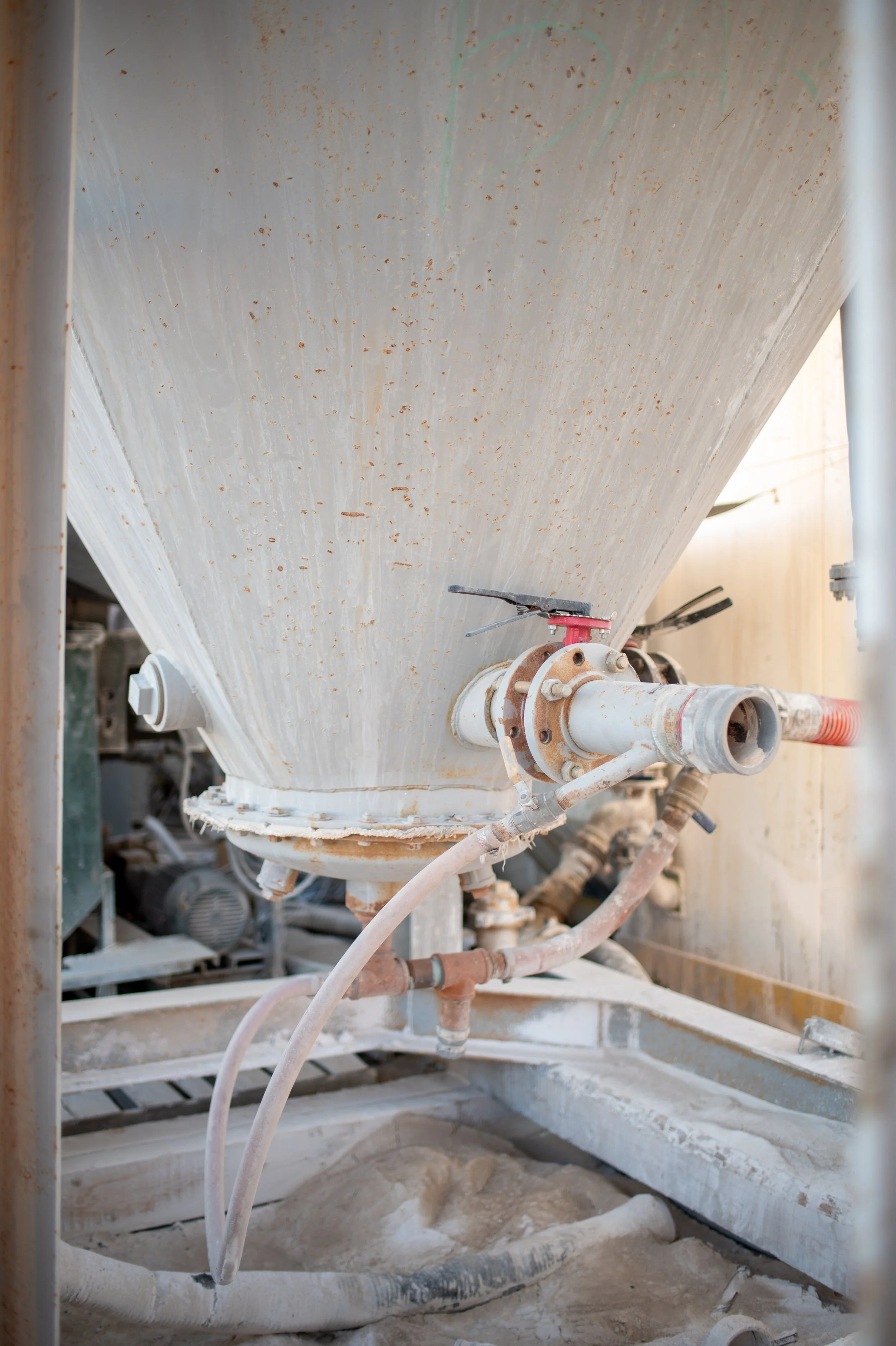 Close-up of a large industrial machine or tank with pipes and valves, covered in a white powdery dust, in an industrial setting.