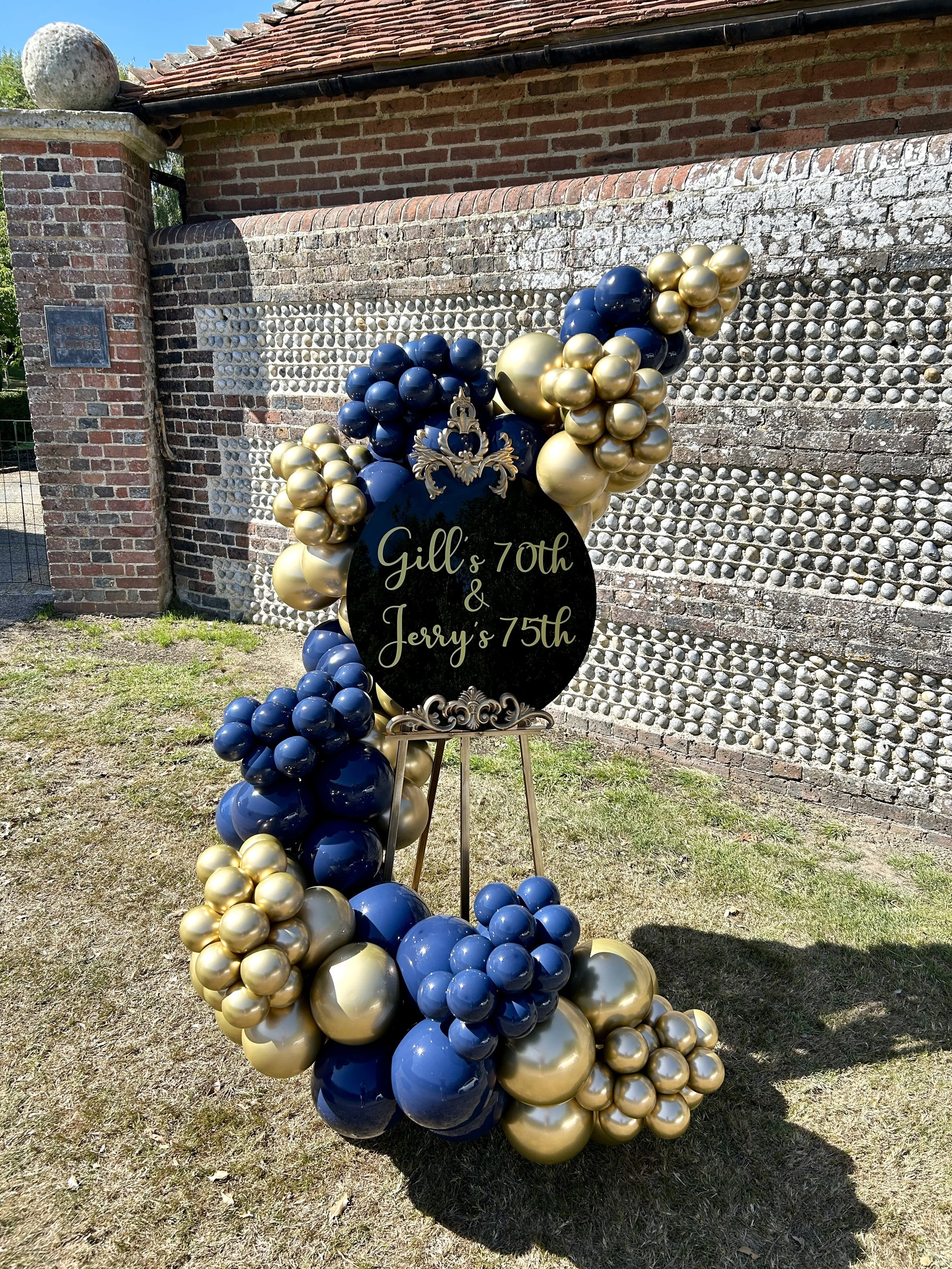 Easel display for a joint 70th and 75th birthday using gold and navy balloons with personalised text on a black acrylic disc