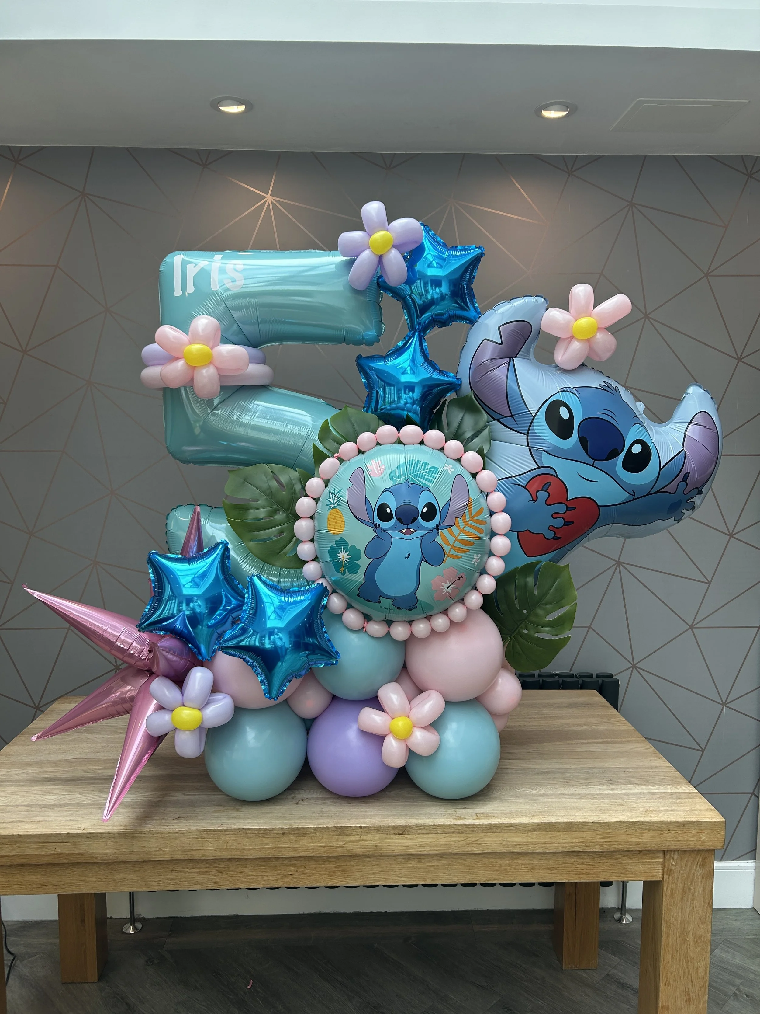 Stitch themed balloon stack for a 5th birthday with blue pink and lilac balloons with added blue stars and foliage