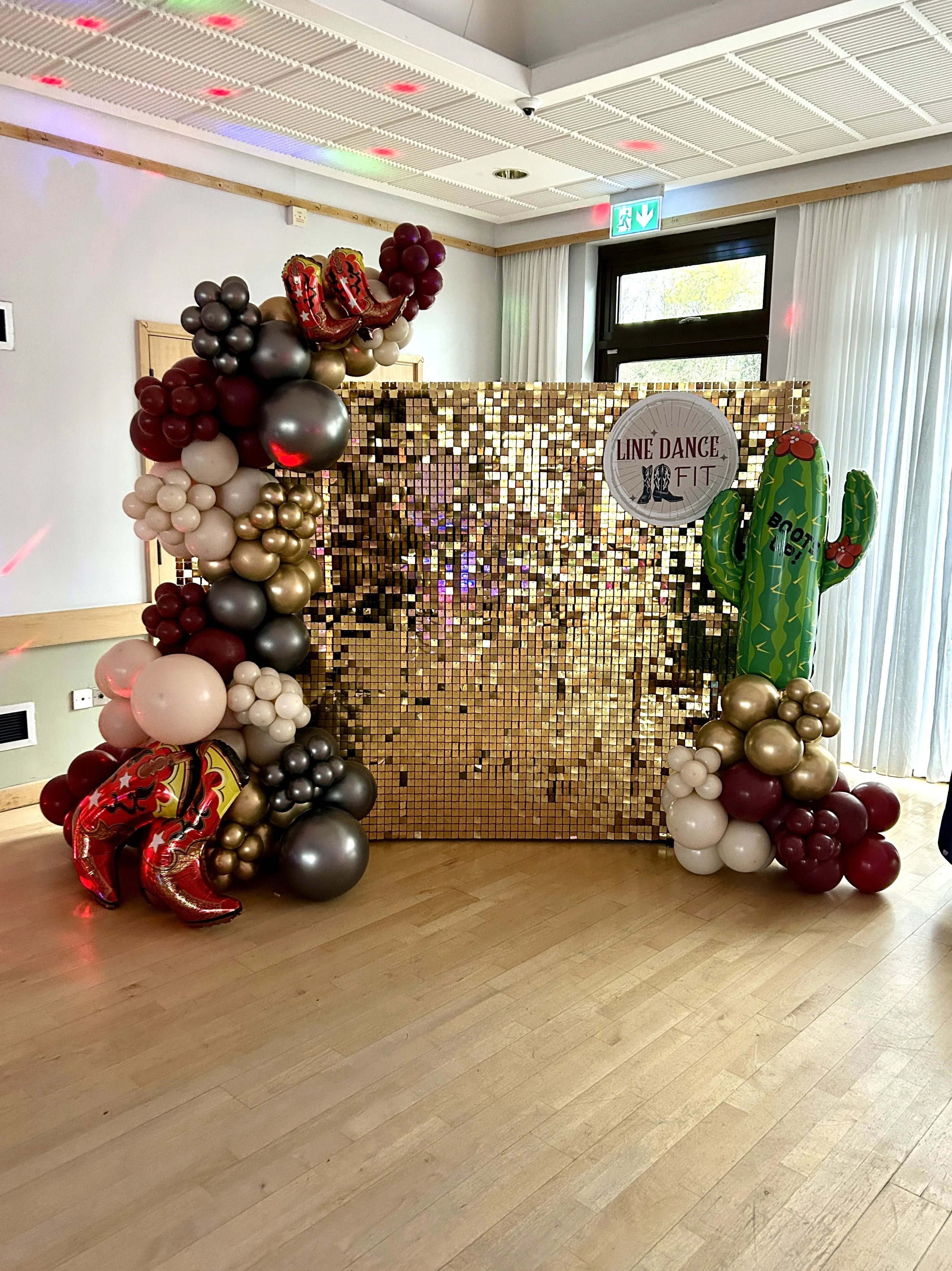 Gold shimmer wall with red grey and cream balloon garland for a line dancing event in east grinstead