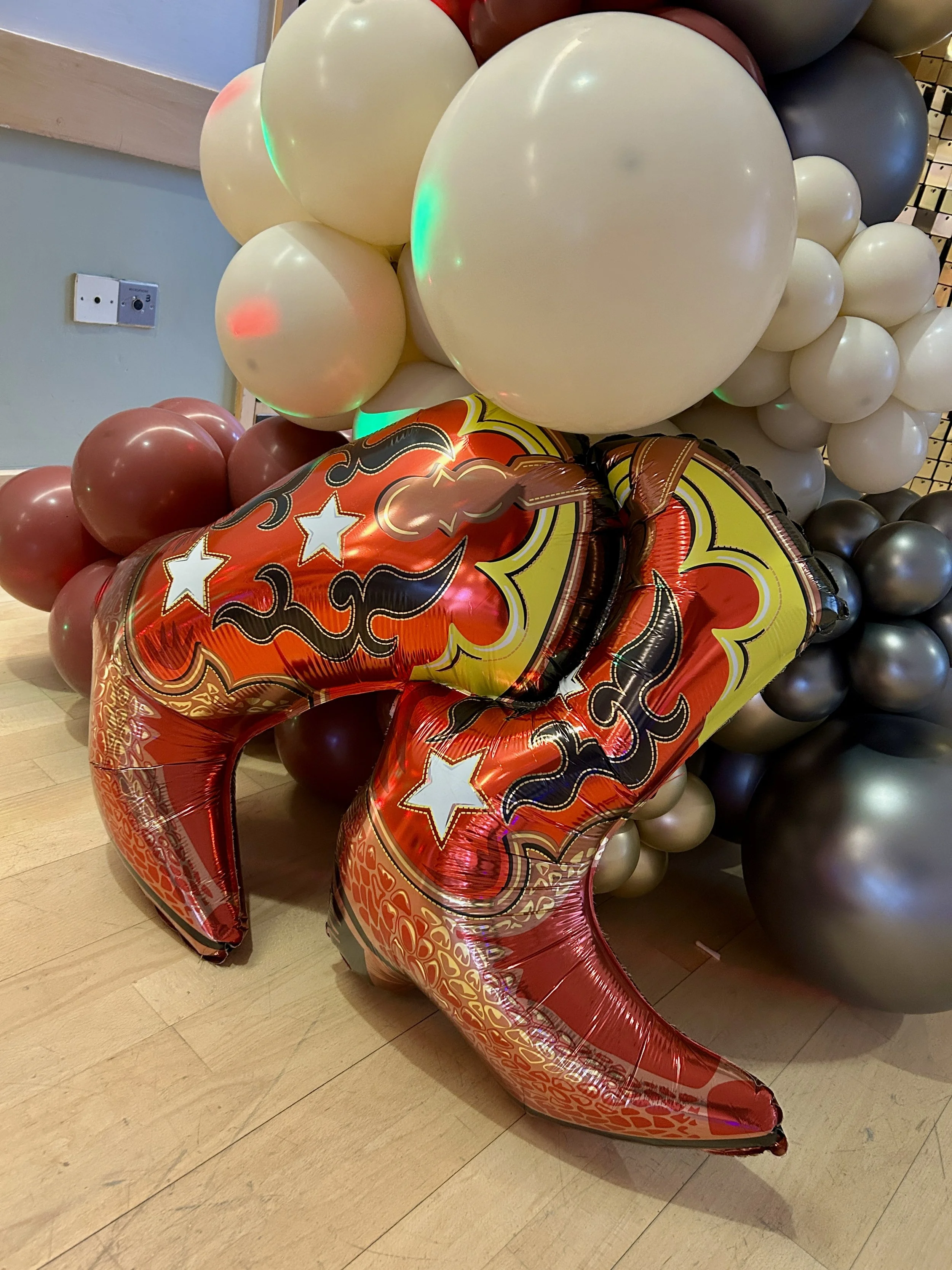 cowboy boot balloons on a balloon garland attached to a gold shimmer wall for a photo backdrop 