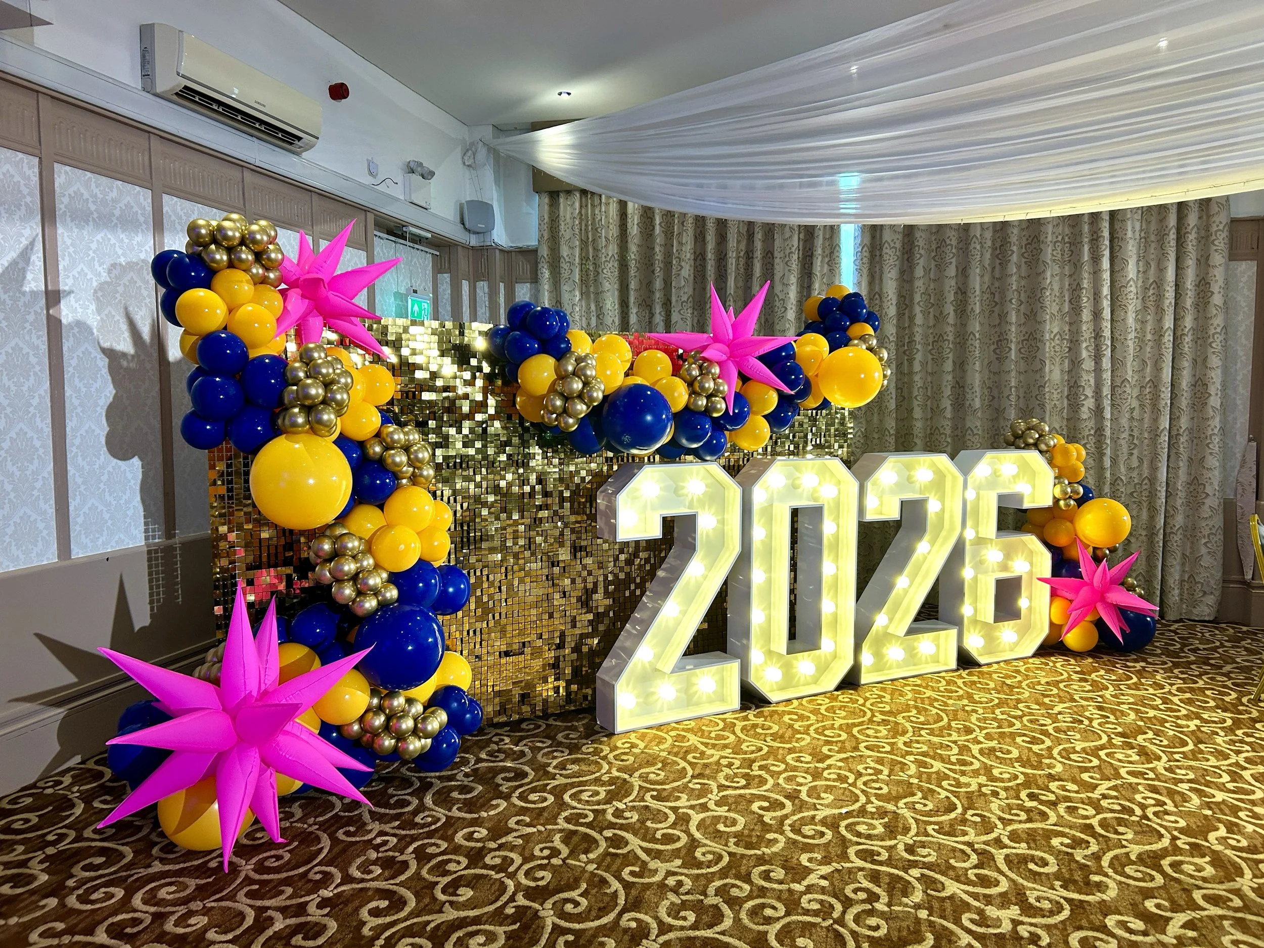 gold shimmer wall with yellow and blue balloon garland and light up numbers for a awards ceromony in east grinstead 