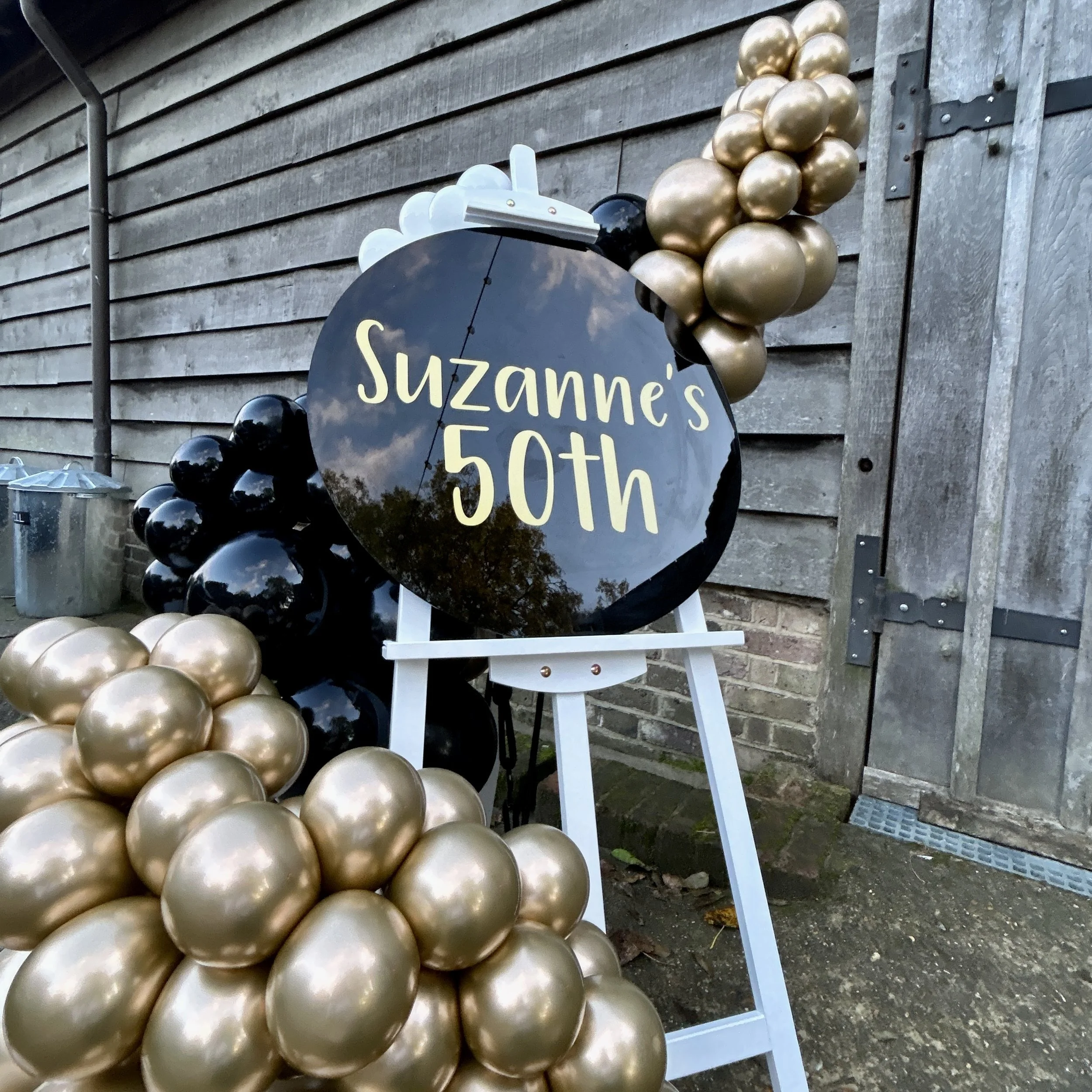 50th birthday easel display with gold and black balloons at the yogurt rooms in east grinstead