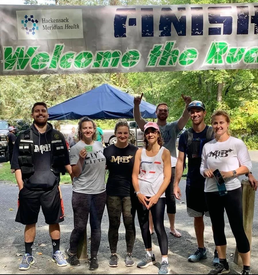 Group of people smiling under a "Finish" banner at an outdoor event.