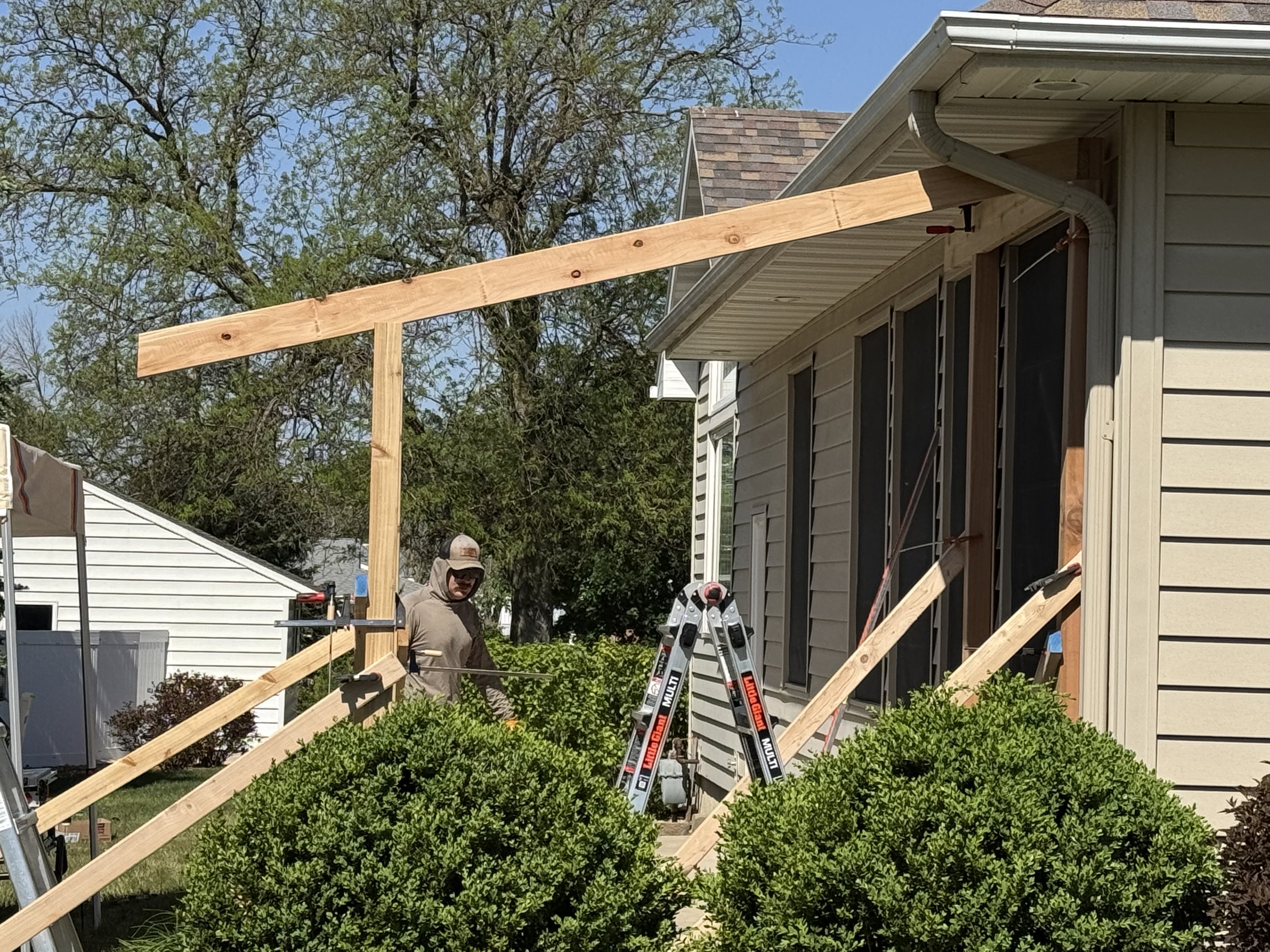 Construction workers building a wooden frame on the side of a house during daytime for a catio and covered patio in Iowa.