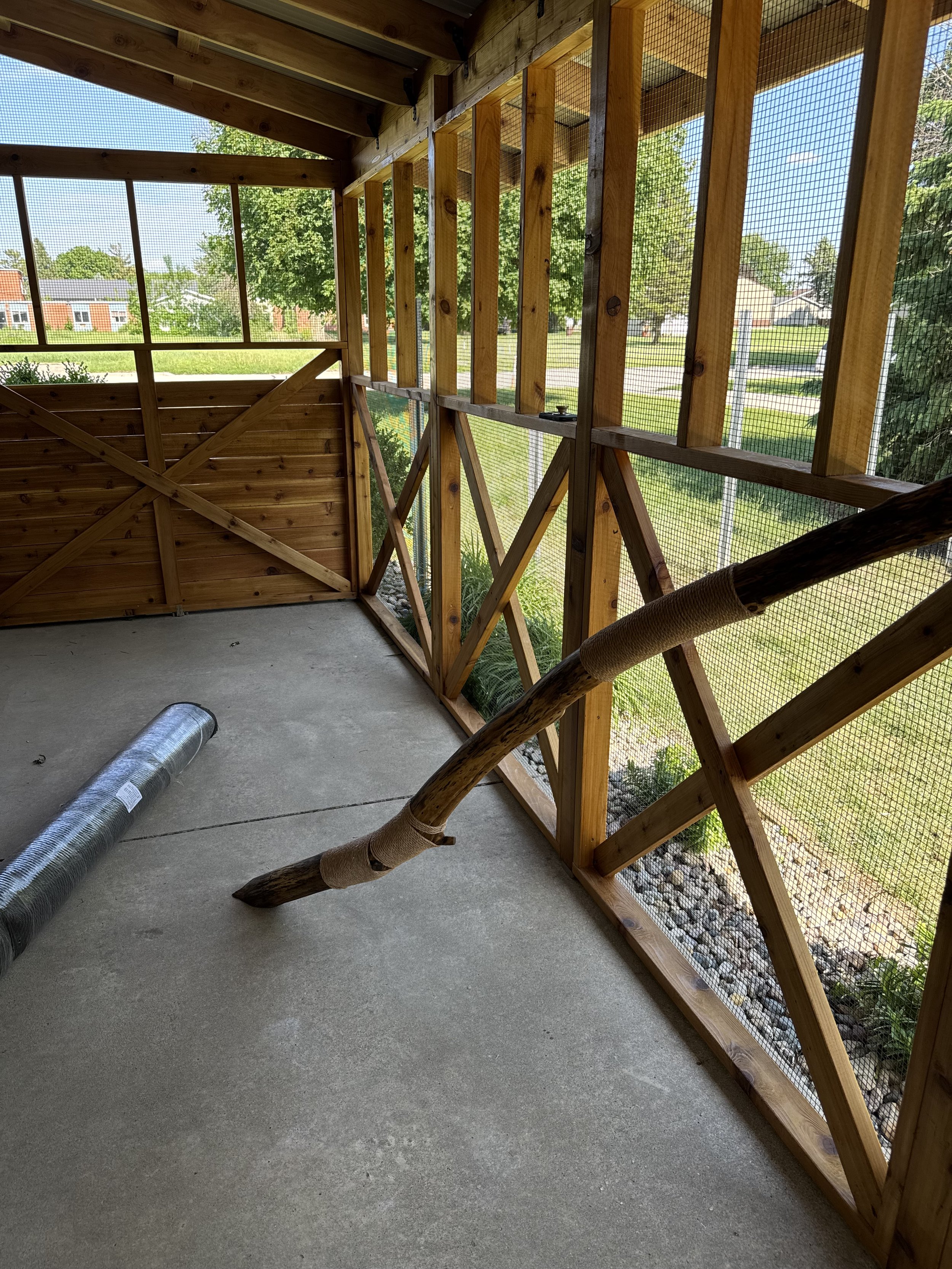 Partially constructed outdoor catio structure with wooden framing, wire mesh panels, and a concrete floor.