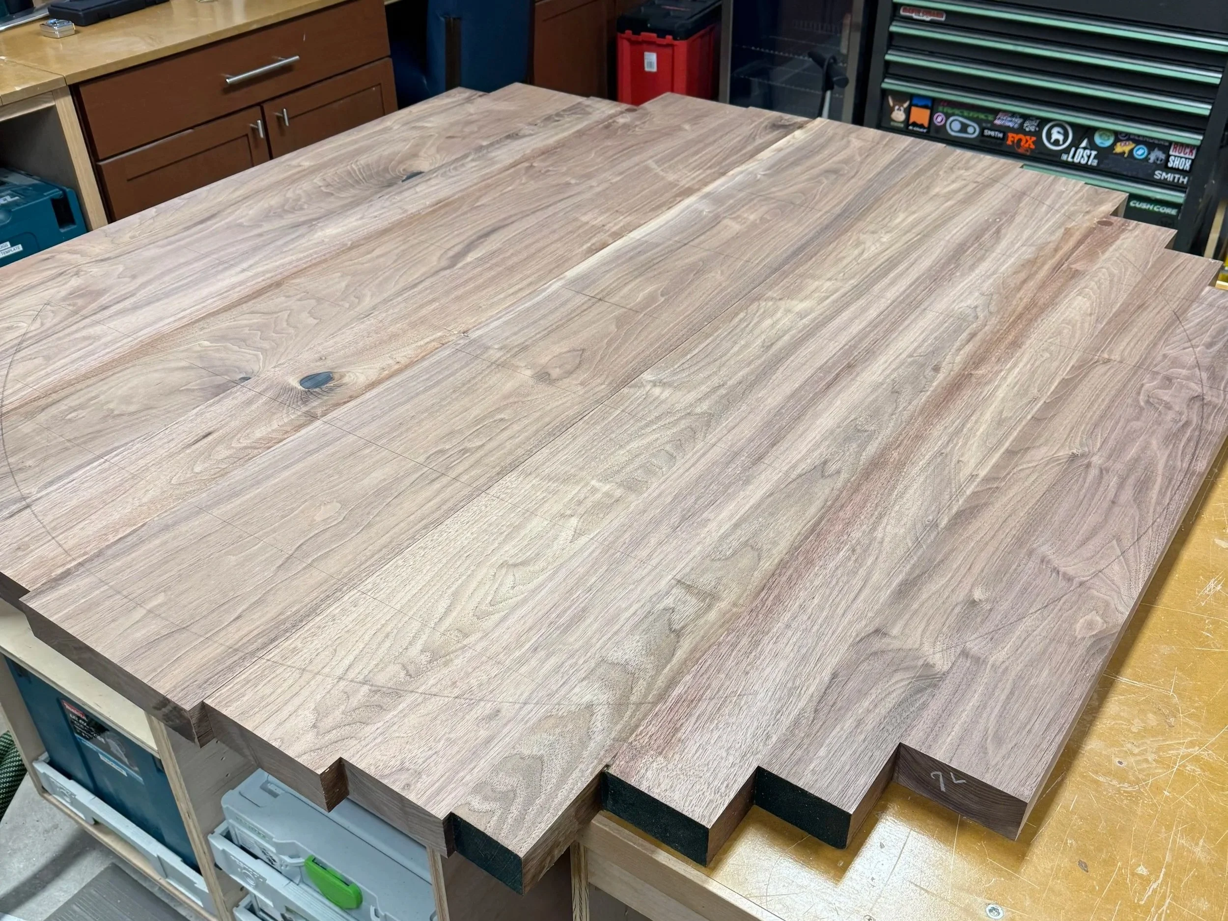 A large stack of light oak wood planks with visible wood grain and knots, placed on a display table ready to be worked on.