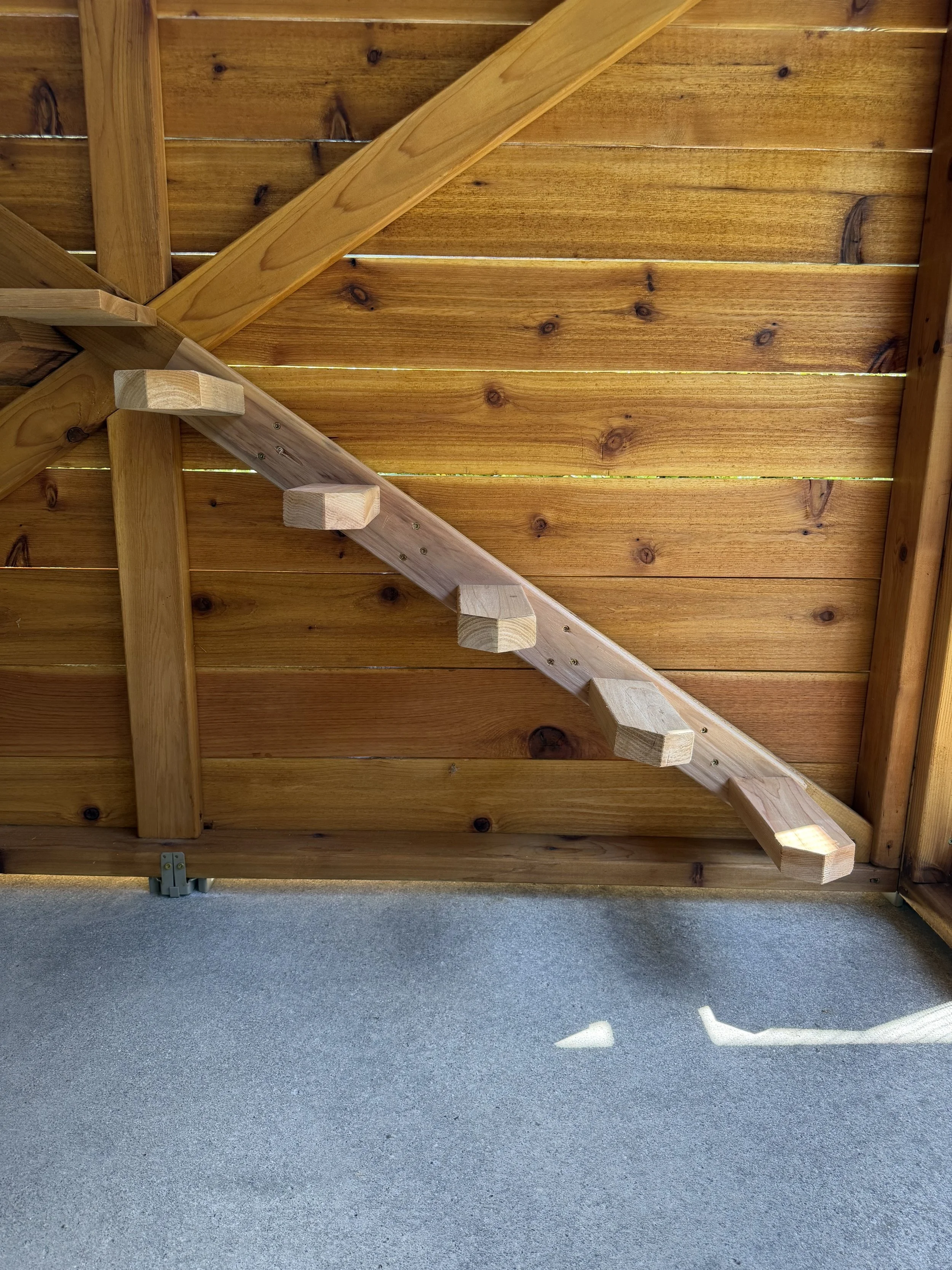 View of a wooden fence with horizontal wooden planks, showing part of a wooden side railing of a staircase for cats to climb on.