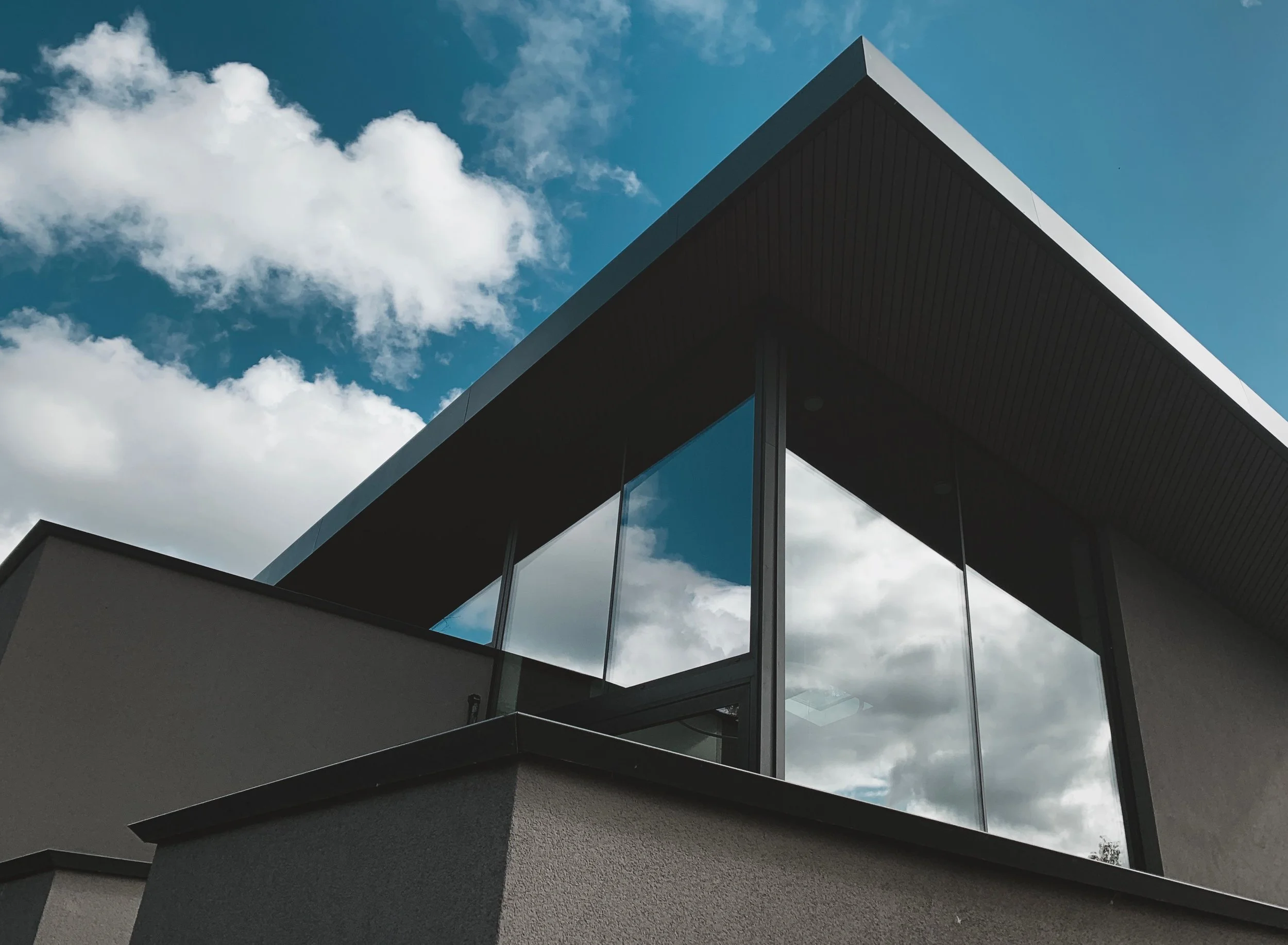 Modern building with large glass windows and sharp angles seen against a blue sky with clouds.