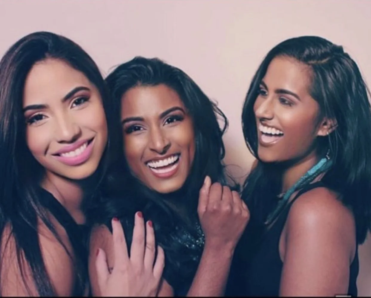 Three women with dark hair smiling and enjoying each other's company, dressed casually.