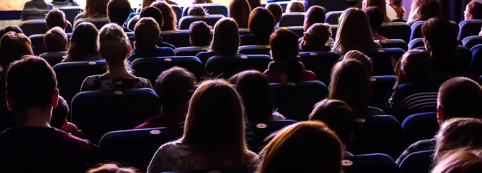 Audience seated in a theater, facing a stage