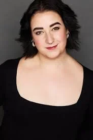 Portrait of a woman with dark hair wearing a black top against a gray background.