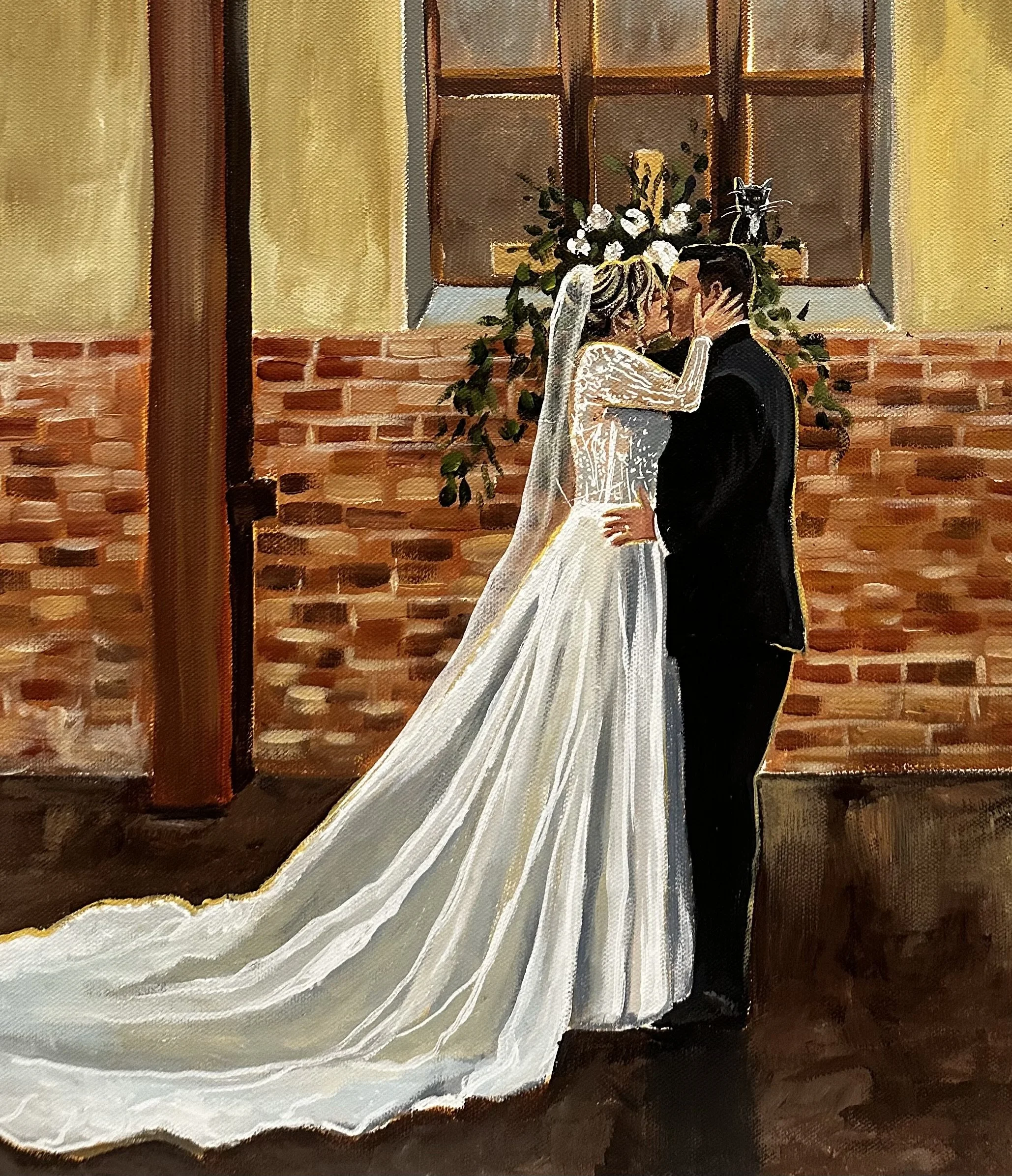 A bride and groom sharing a kiss in an indoor setting, with a floral arrangement and a cat on a ledge behind them.