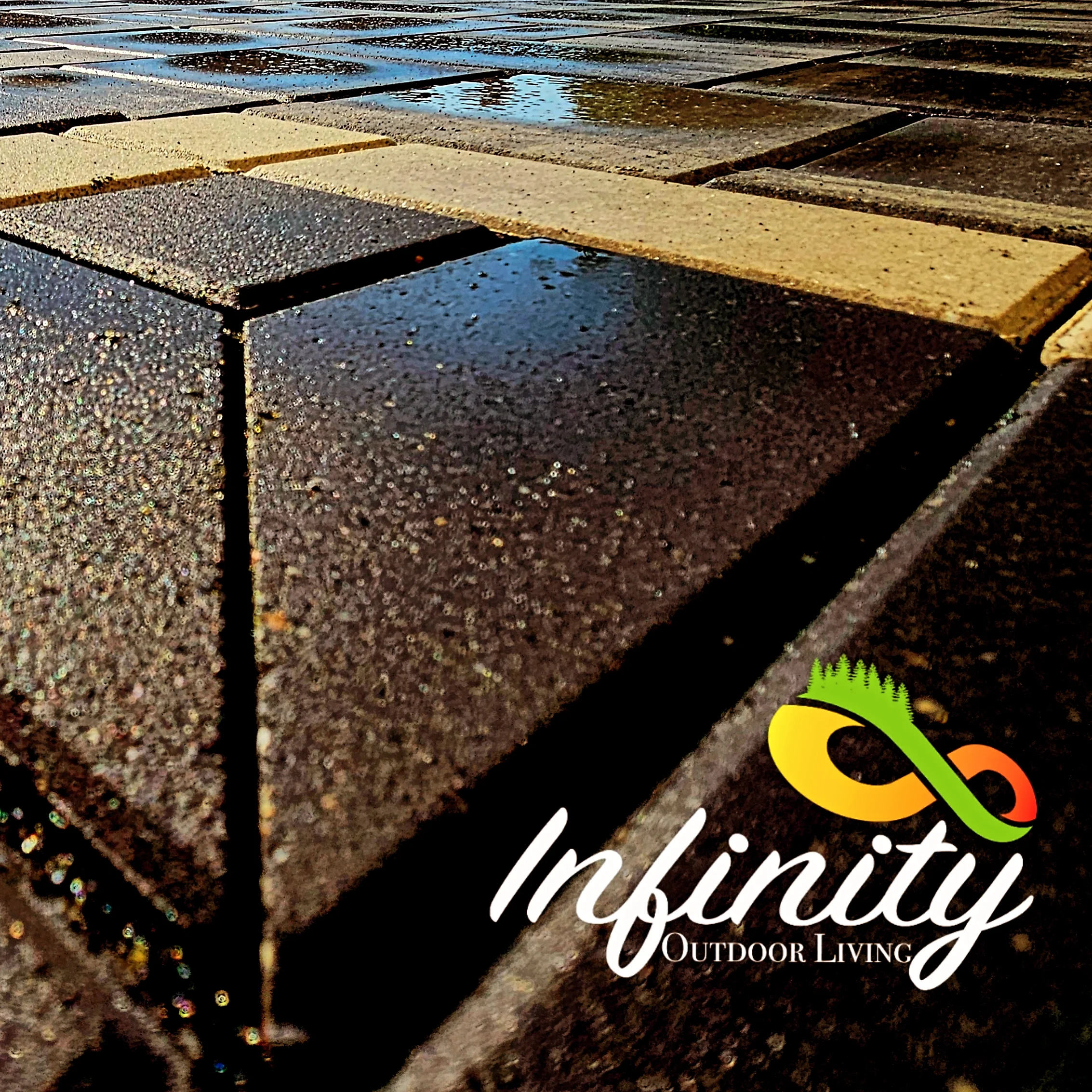 Close-up of wet brick and concrete sidewalk with a small puddle reflecting sky. In the bottom right corner, a logo features a green, orange, and yellow infinity symbol with tree-like elements, along with the text 'Infinity Outdoor Living'.