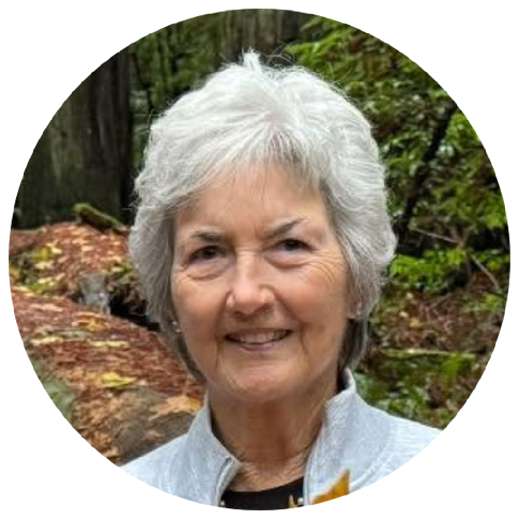 Portrait of an elderly woman with short gray hair, smiling outdoors among trees and foliage.