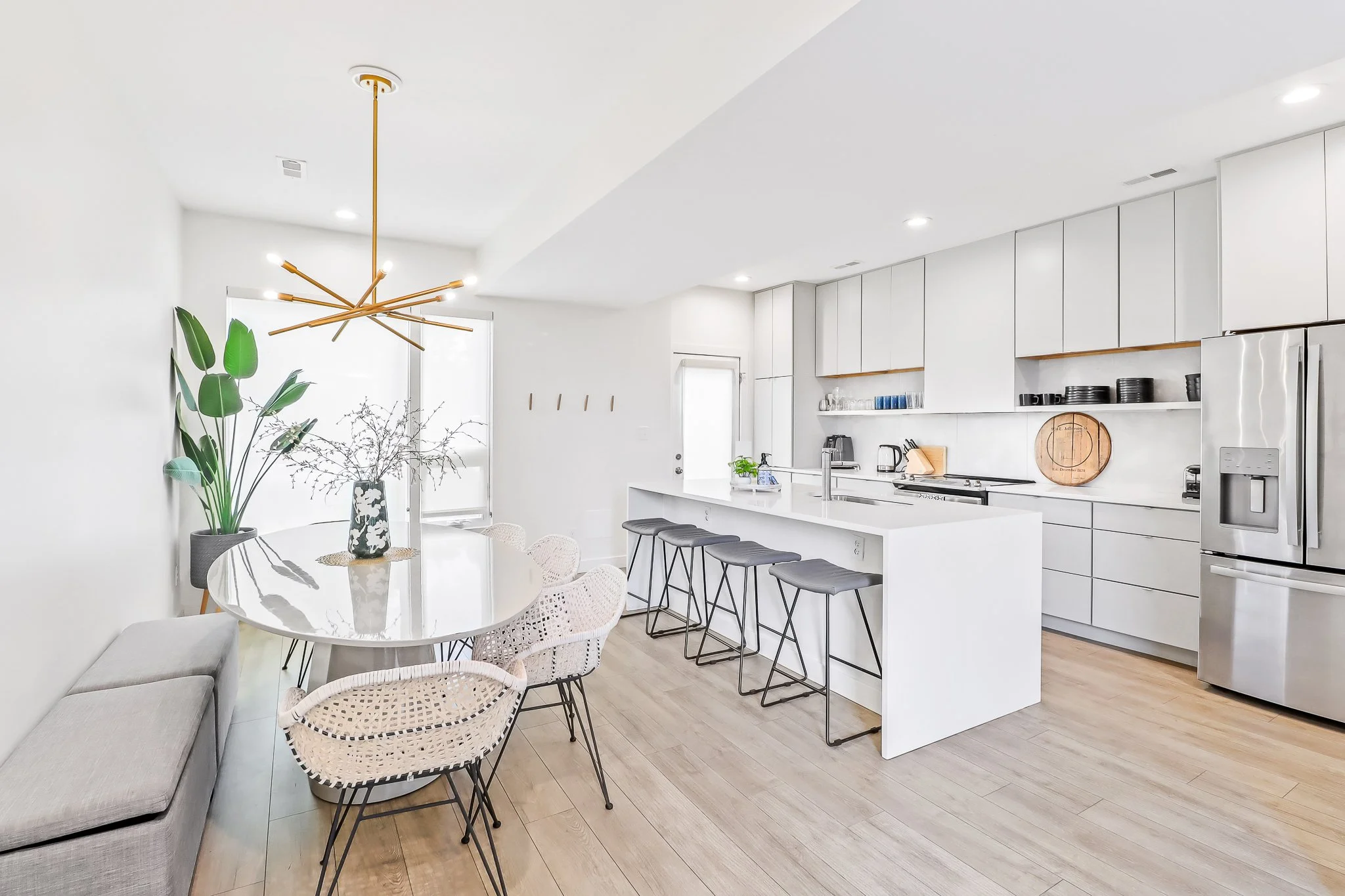 Bright and modern open-concept kitchen with a white waterfall island and a dining area with a contemporary chandelier, professionally photographed for a real estate listing.
