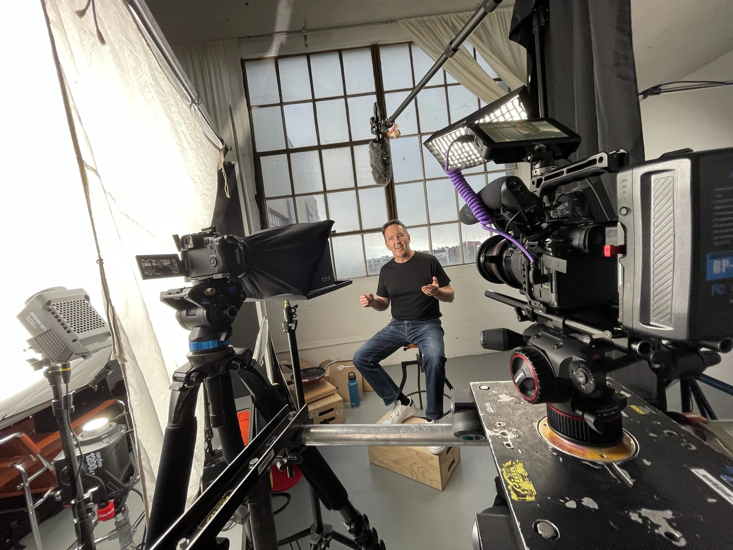 Swope Films director and creative director, David Swope, is sitting and speaking to a camera in a studio with cameras, lights, and microphones around him.