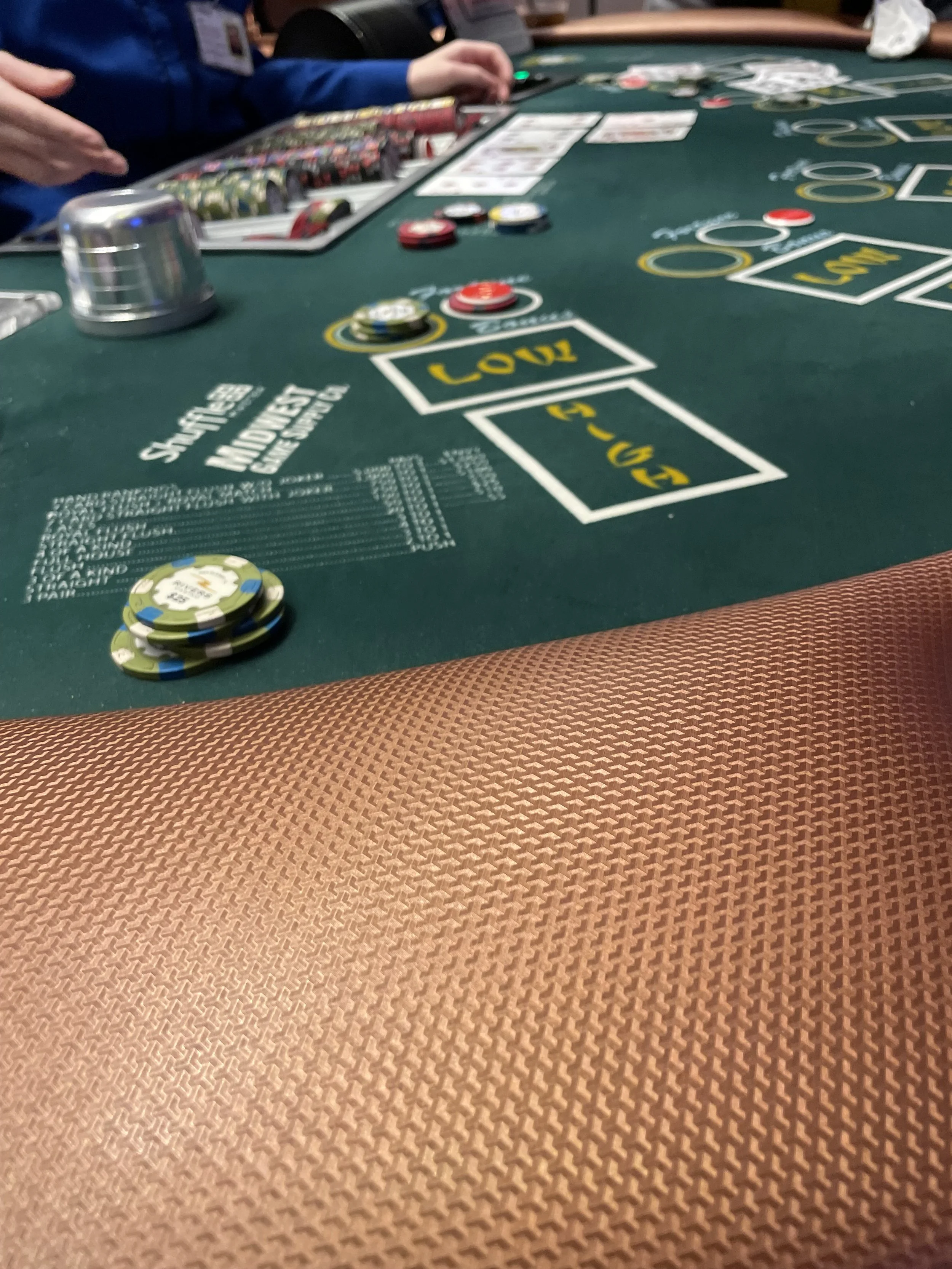 Black felt casino blackjack table with poker chips, cards, and betting areas, with hands of players visible.