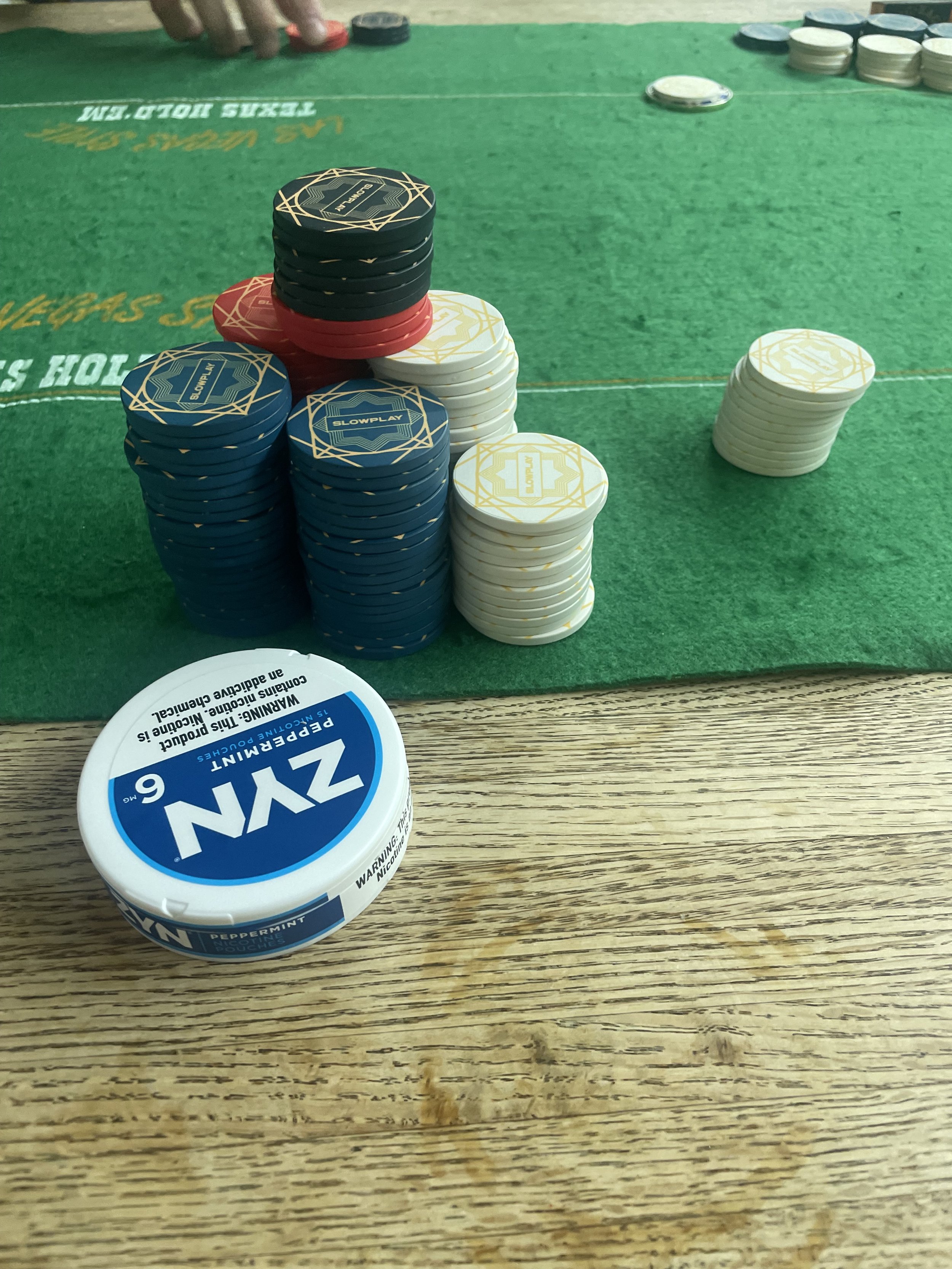 Poker chips of various colors stacked on a green felt poker table, with a tin of Wintergreen chewing gum on a wooden surface in the foreground.