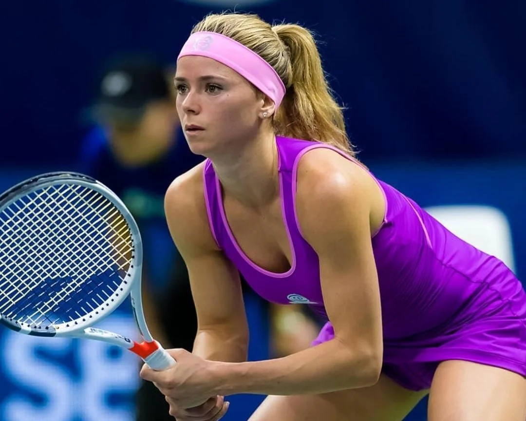 Female tennis player in purple sportswear and pink headband holding a tennis racket during a match.