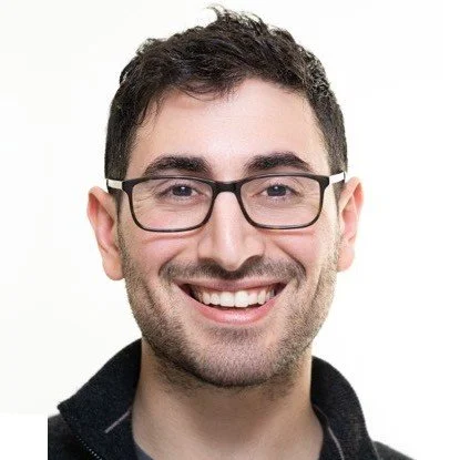 A smiling man with dark hair, glasses, and a beard against a plain white background.