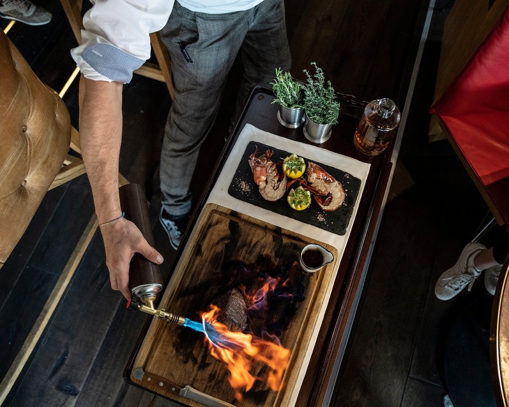Steak wird am Tisch flambiert und auf dem Holzbrett tranchiert