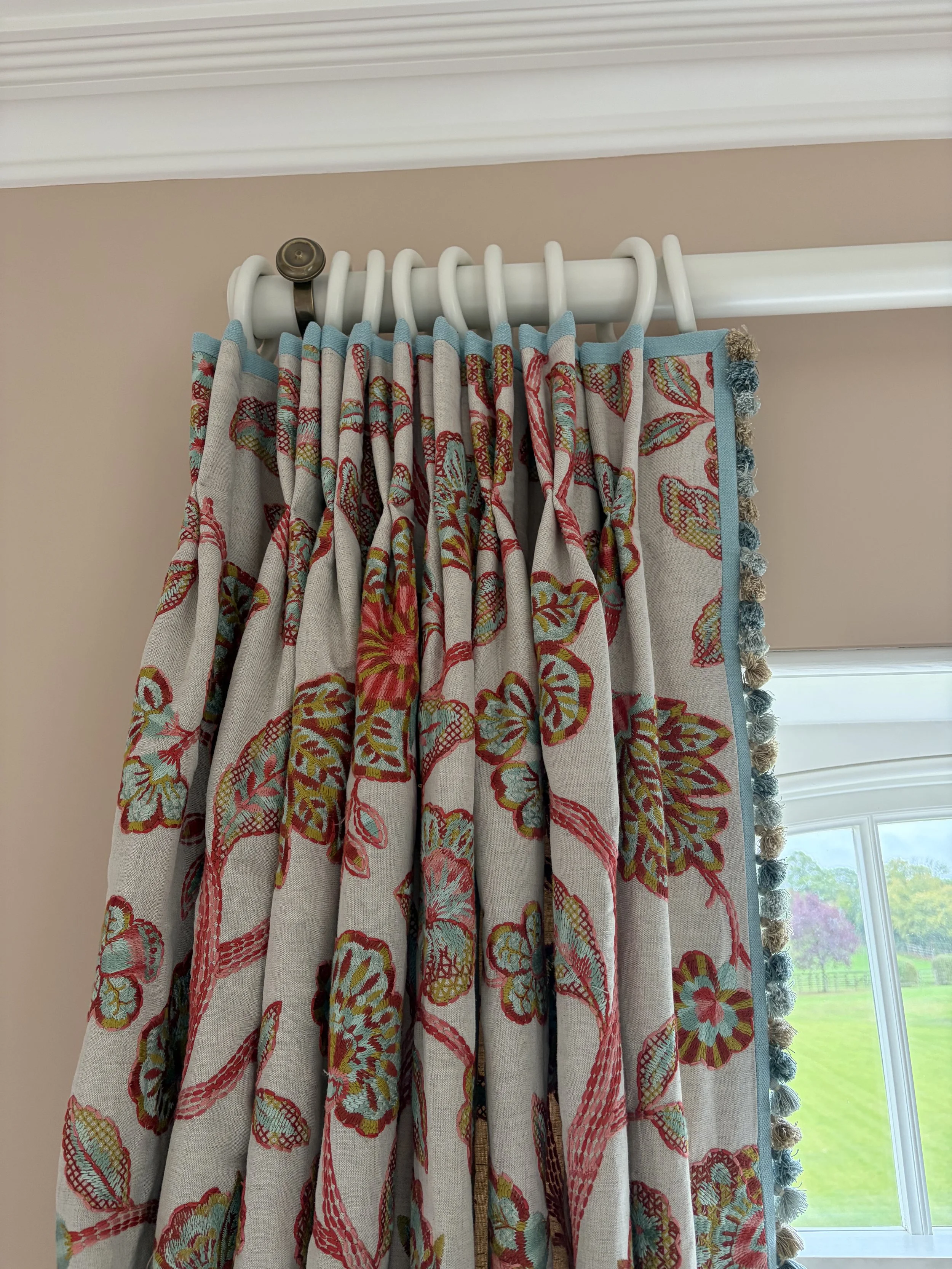 Pinch-pleated embroidered floral curtain with a blue contrast border and bobble trim on a painted pole