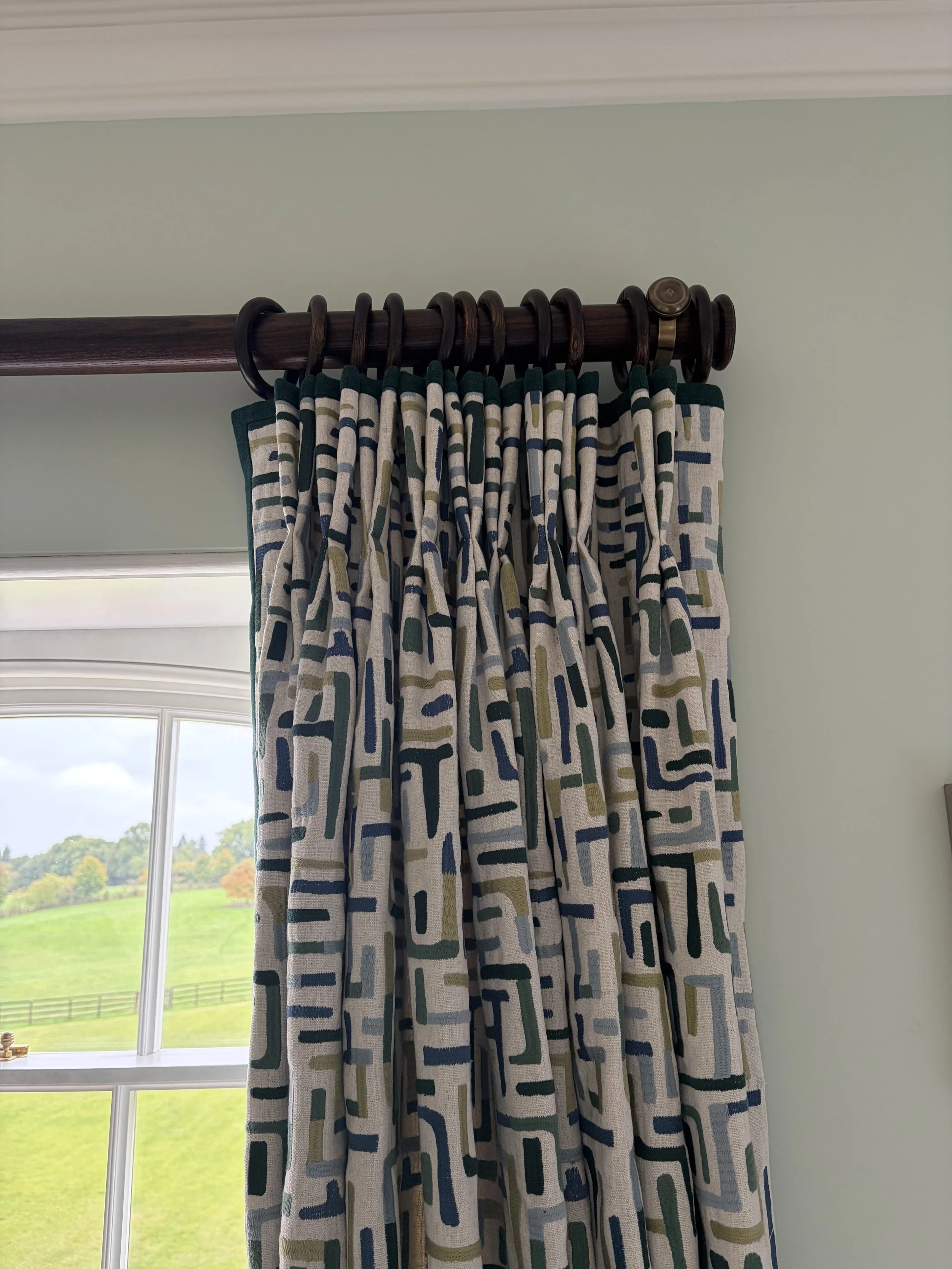 Pinch-pleated curtains in a blue and green geometric print on a dark wooden pole