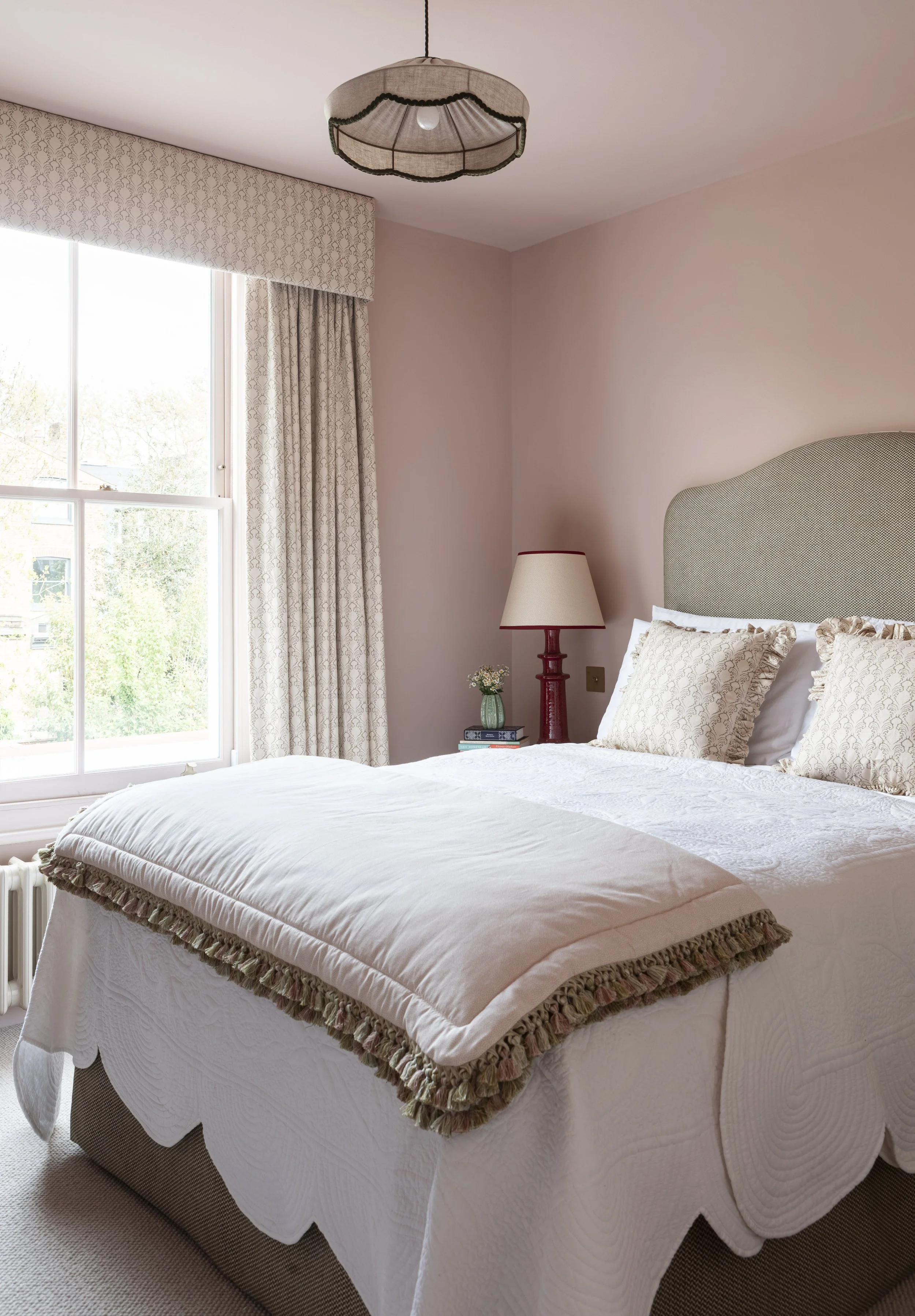 Bedroom curtains in Soane fabric and upholstered pelmet in a pink room, with a scalloped bedspread by Sarah K