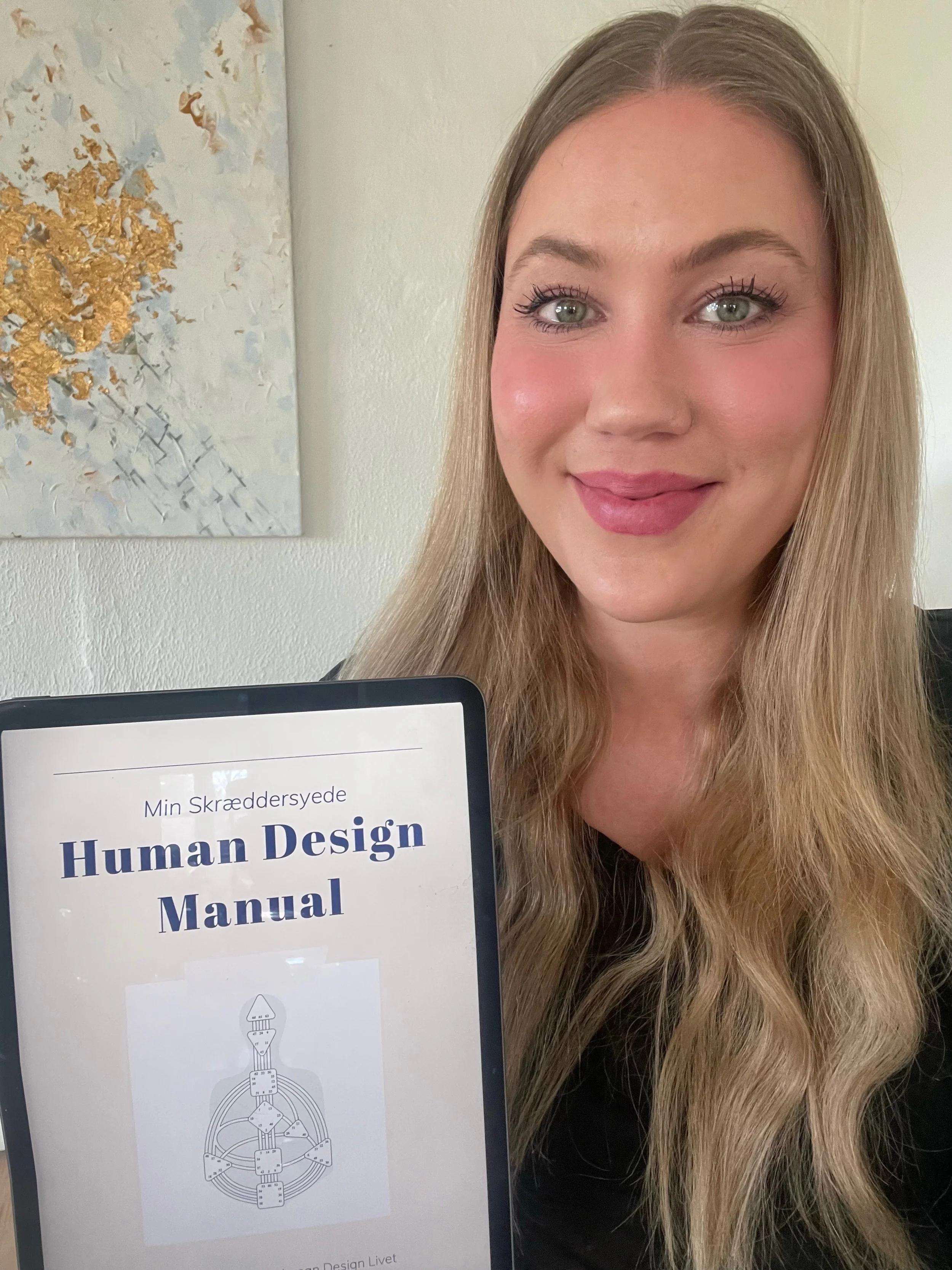 Et smilende kvinde med langt, blond hår, der holder et digitalt device med en manual til menneskedesign.