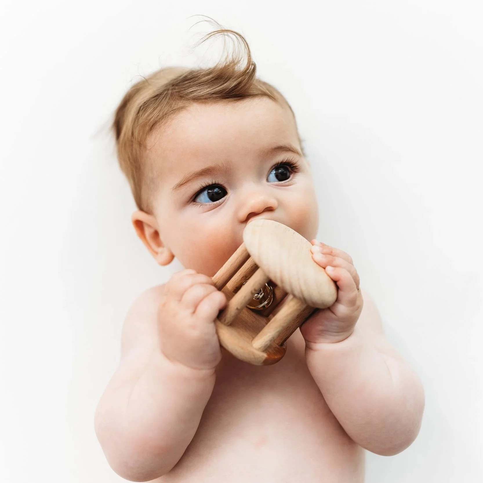 Baby holding and chewing on a wooden toy with minimal background.