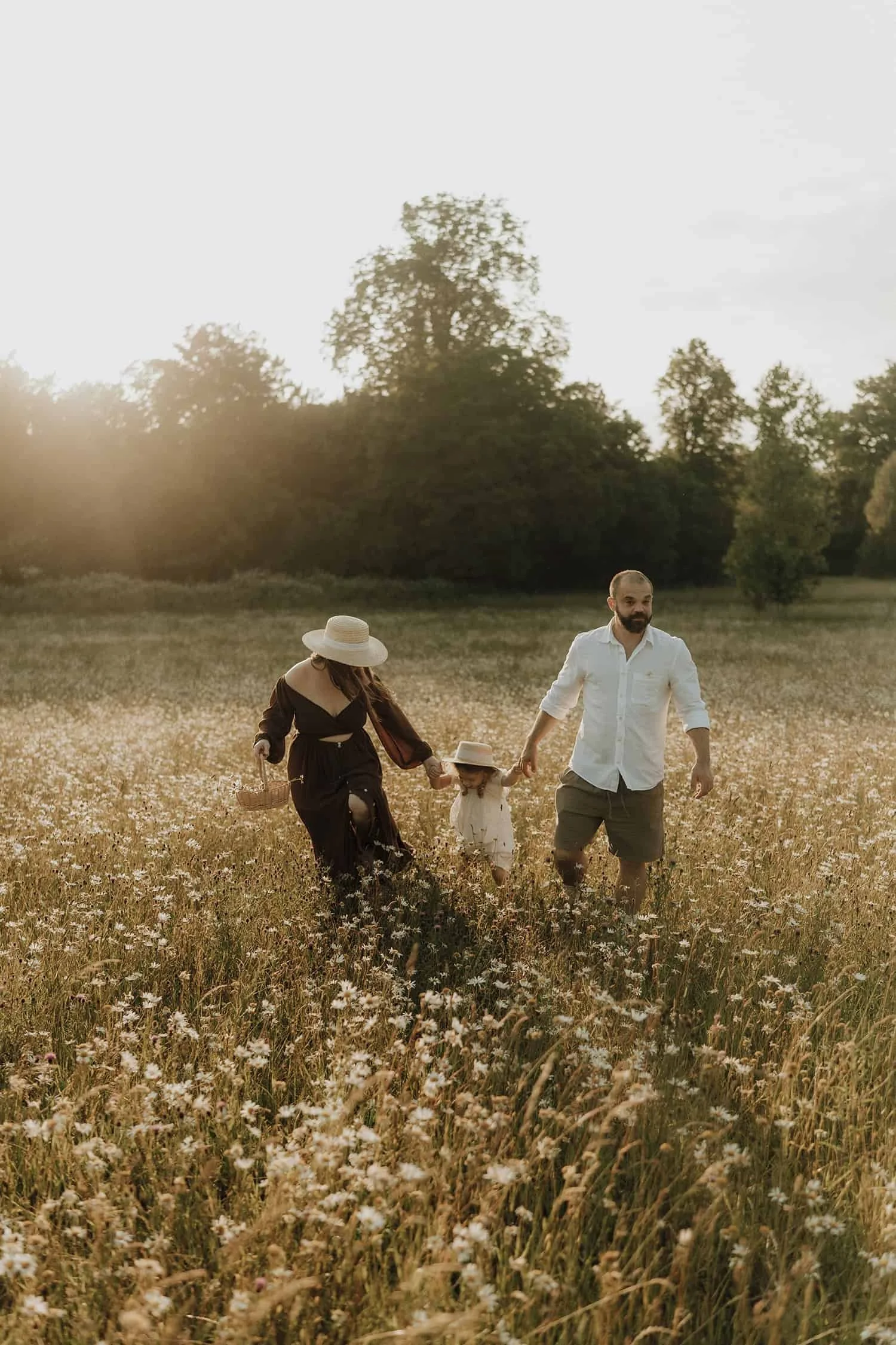 A family of four walking through a field of wildflowers at sunset, holding hands and smiling.