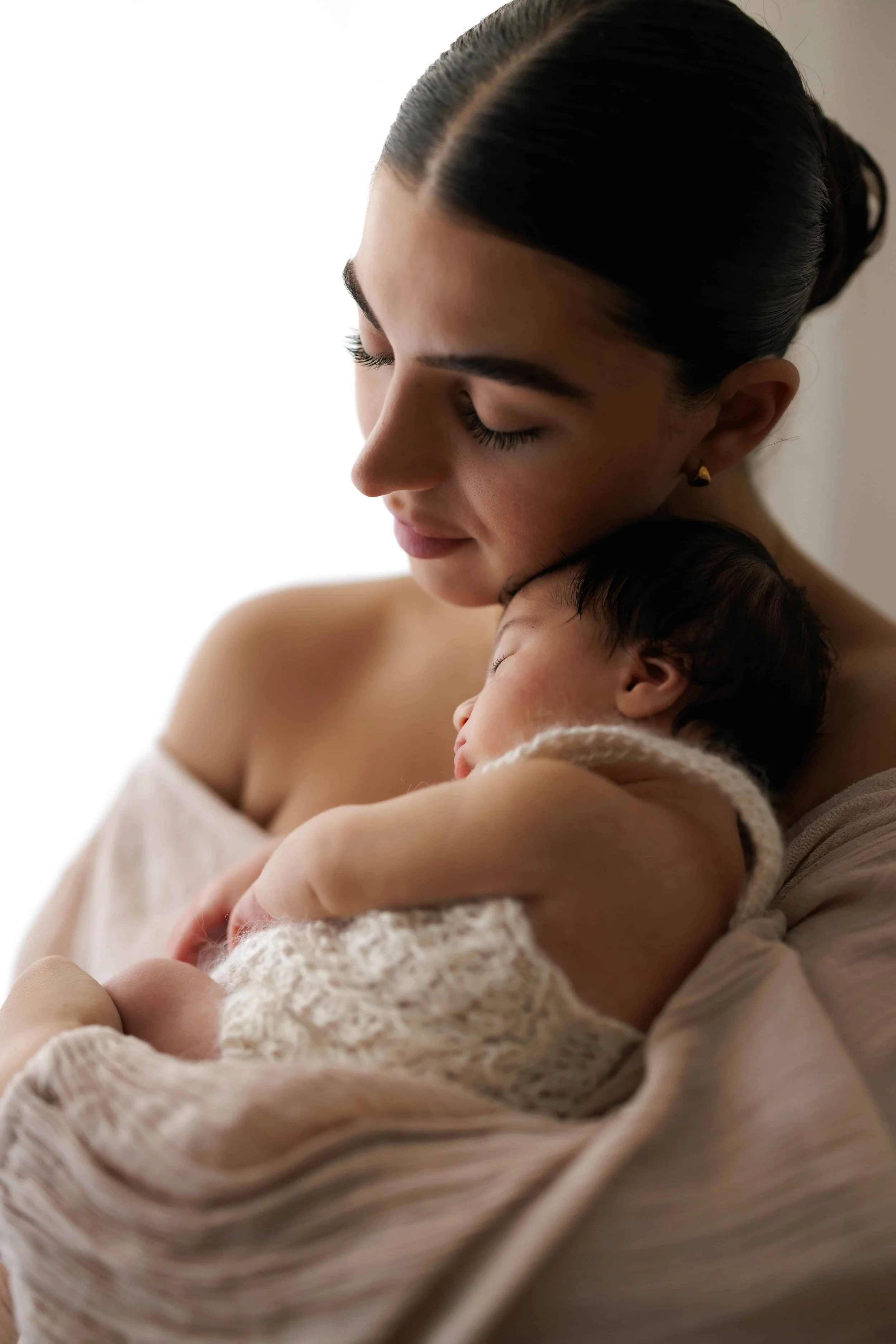 A woman with dark hair in a bun holds a sleeping baby wearing hand knitted romper